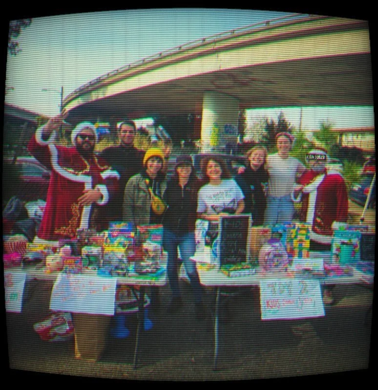 Group of people selling decorated cakes at an outdoor holiday event under a bridge