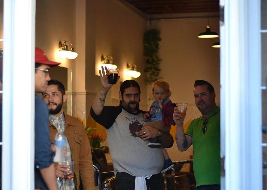 Group of men and a young girl holding drinks inside a restaurant, with one man holding a child and raising his glass.