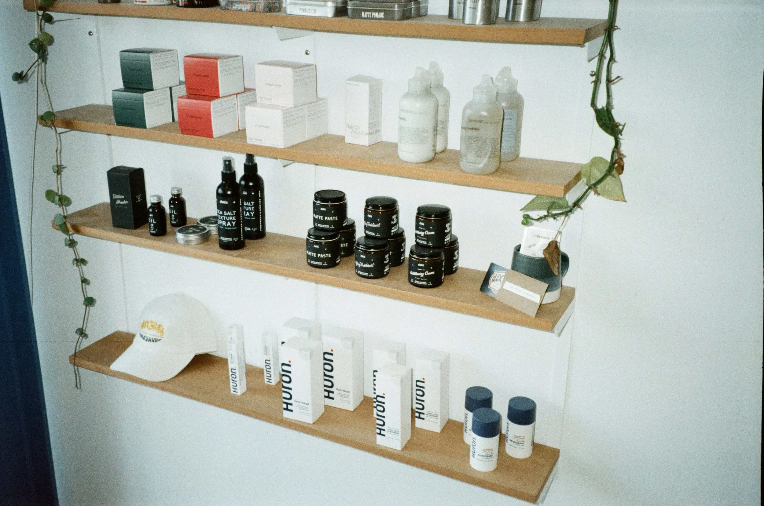 Wooden shelves with haircare products, including boxes, bottles, and jars, organized neatly. Green vines drape along the side of the shelves.