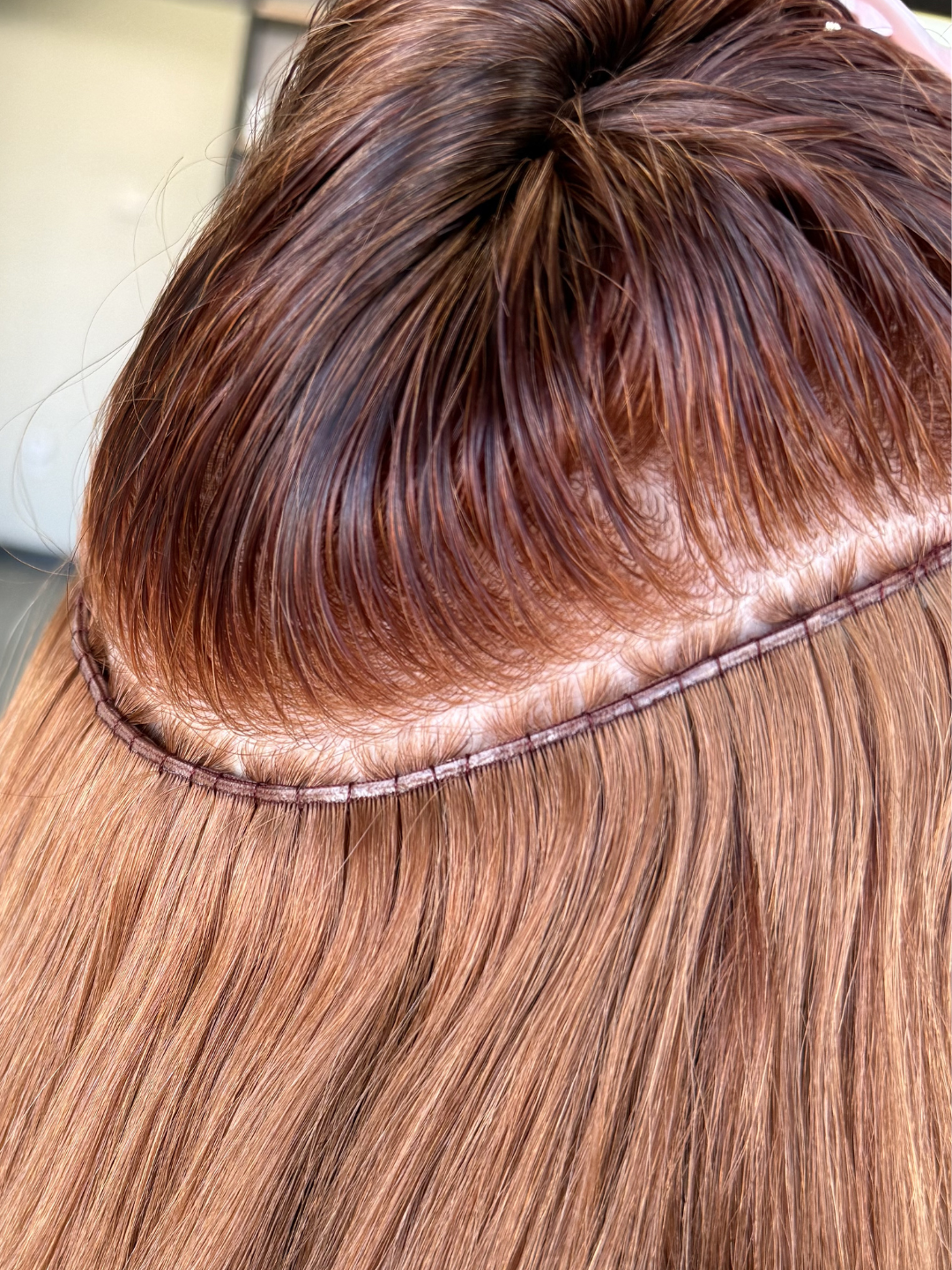 Close-up of a person with long, red hair showing the details of a row of beaded row, sewn in hair extensions. 