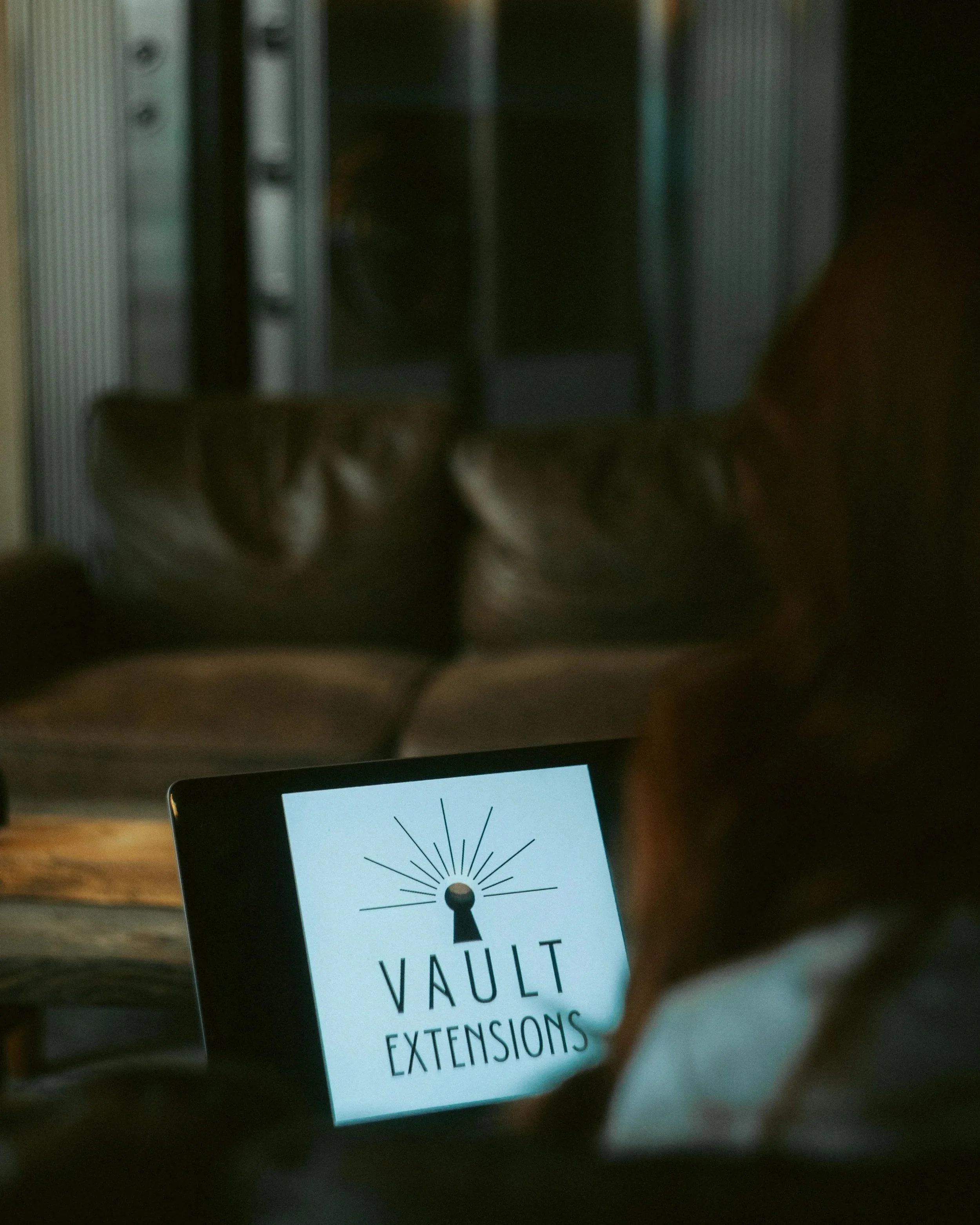 Close-up of a laptop displaying a logo with a stylized vault and rays extending outward, with the words 'VAULT Extensions'