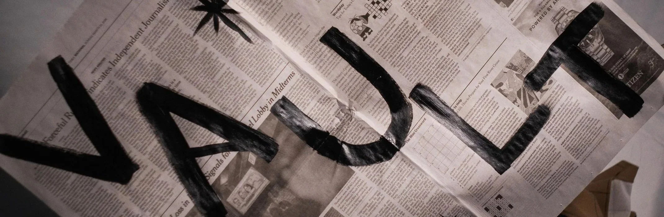 Black letters spelling the word 'Vault' painted on a newspaper-covered surface.