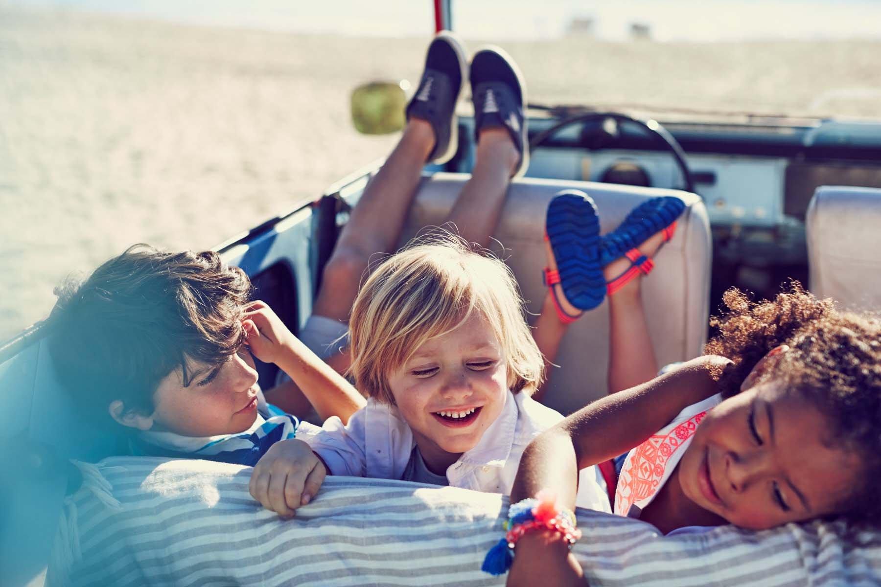 Group of children lying on a blanket on the back of a vehicle, enjoying a sunny day at the beach or a park.