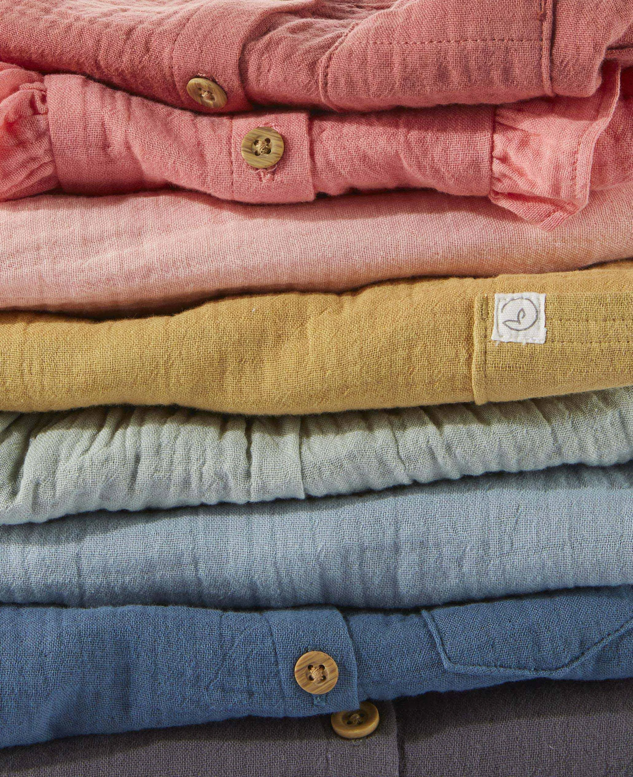 Stacked folded linen product  in shades of pink, blue, gray, and yellow with wooden buttons.