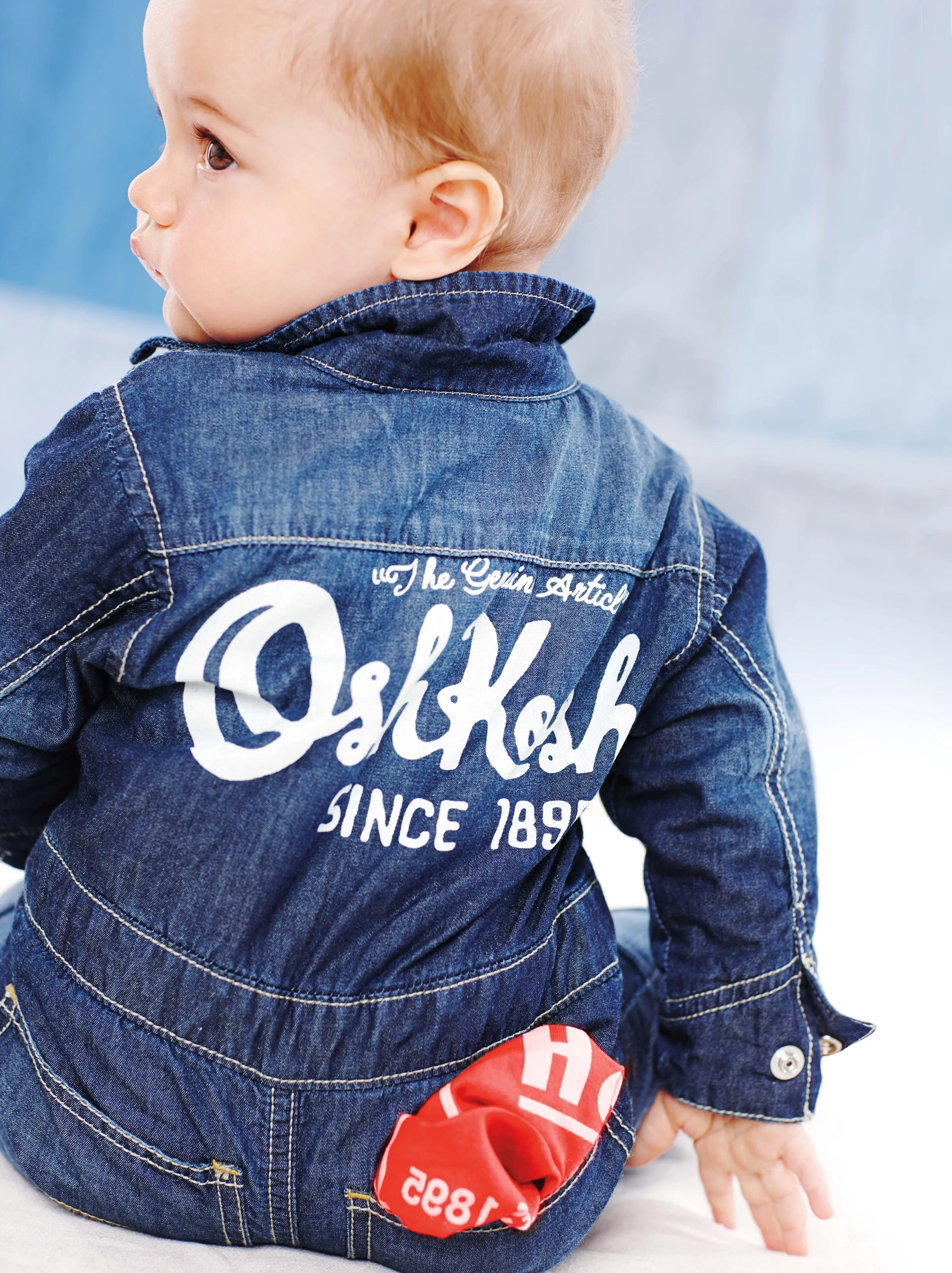 Close-up of a young child with fair skin, light blonde hair, and brown eyes wearing a dark blue denim jacket with white embroidered text on the back.