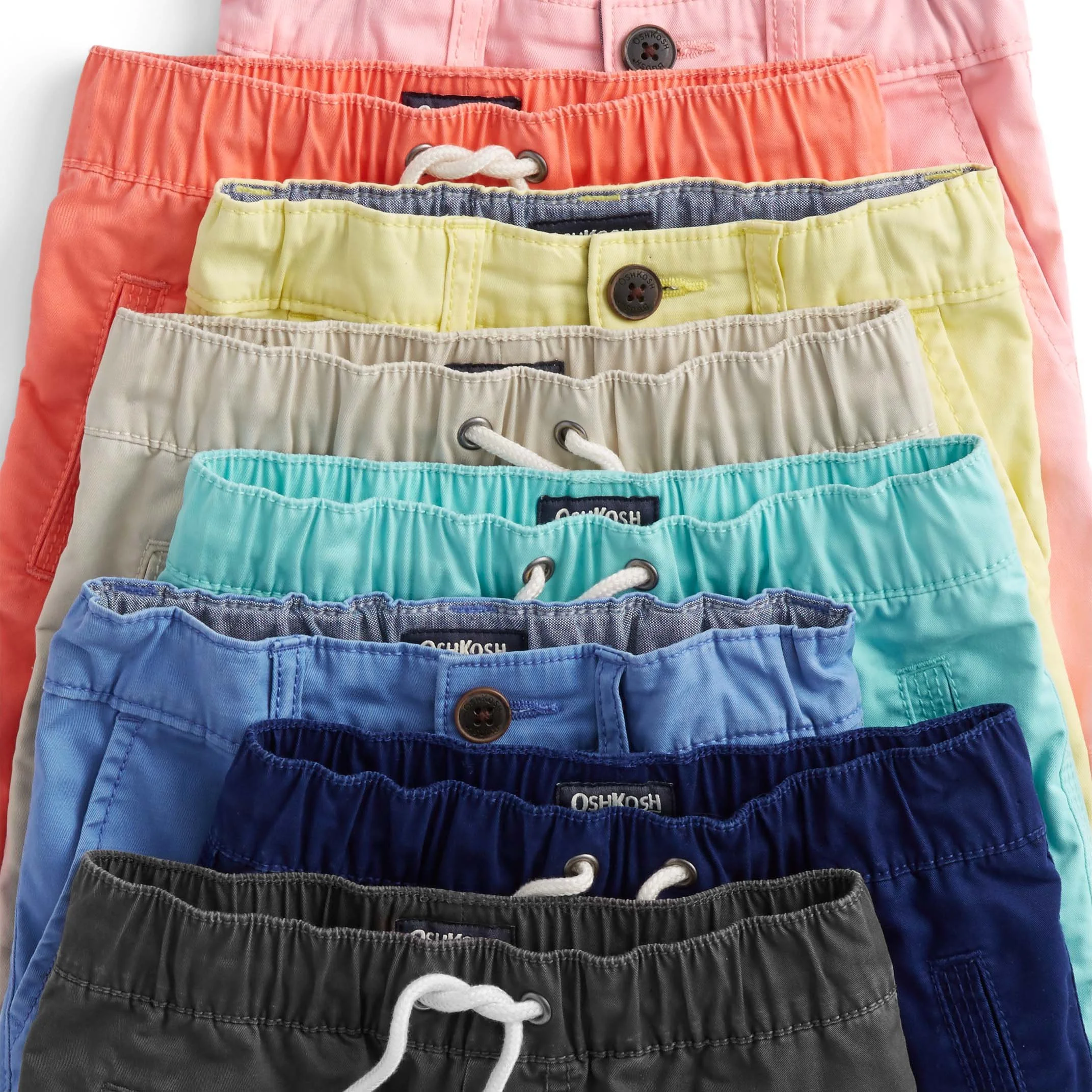 Colorful stack of shorts in pink, coral, yellow, white, blue, and black, each with a button and drawstring, arranged from top to bottom.
