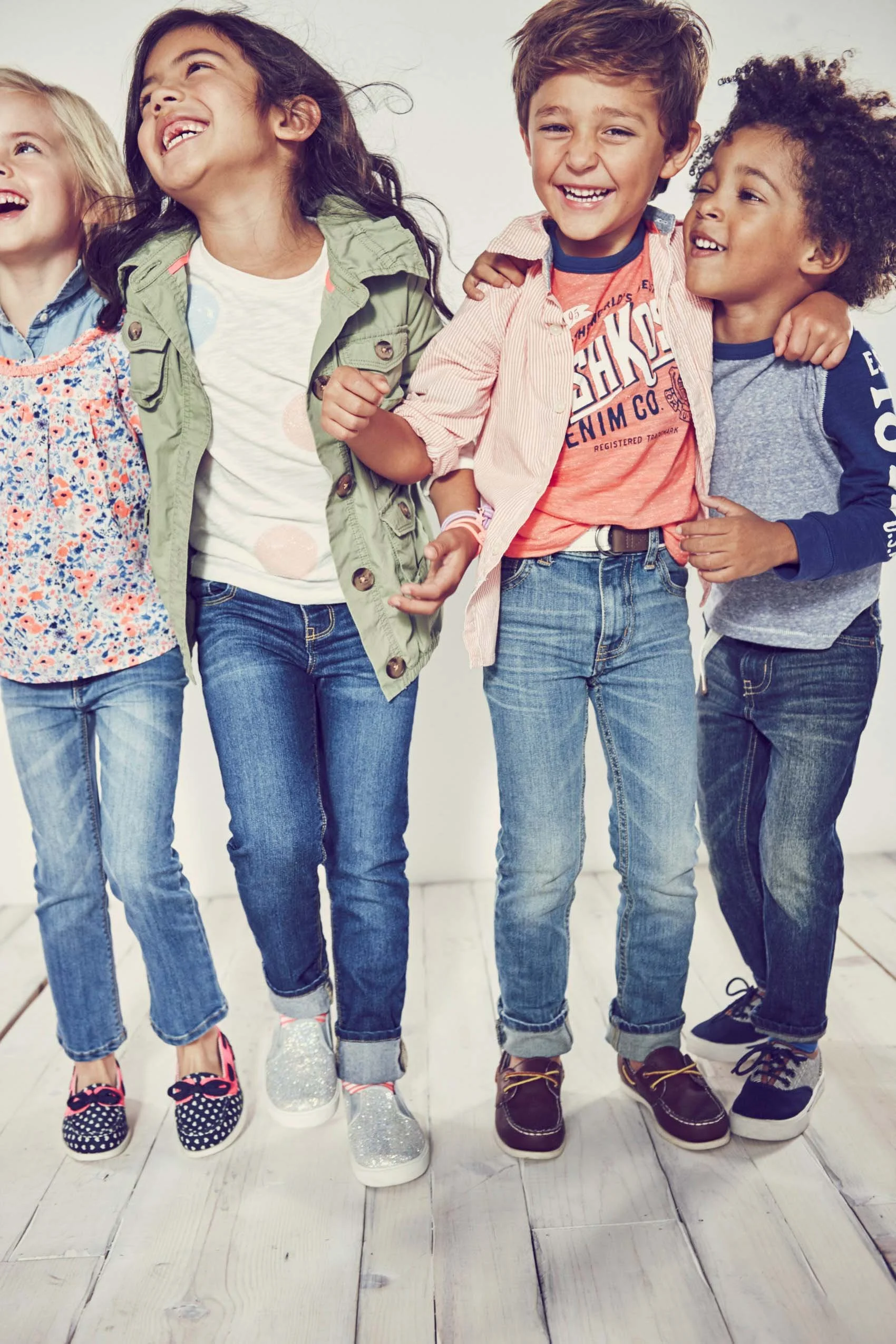 Close-up of four children's legs and feet standing side by side on white wooden floor, wearing colorful sneakers.