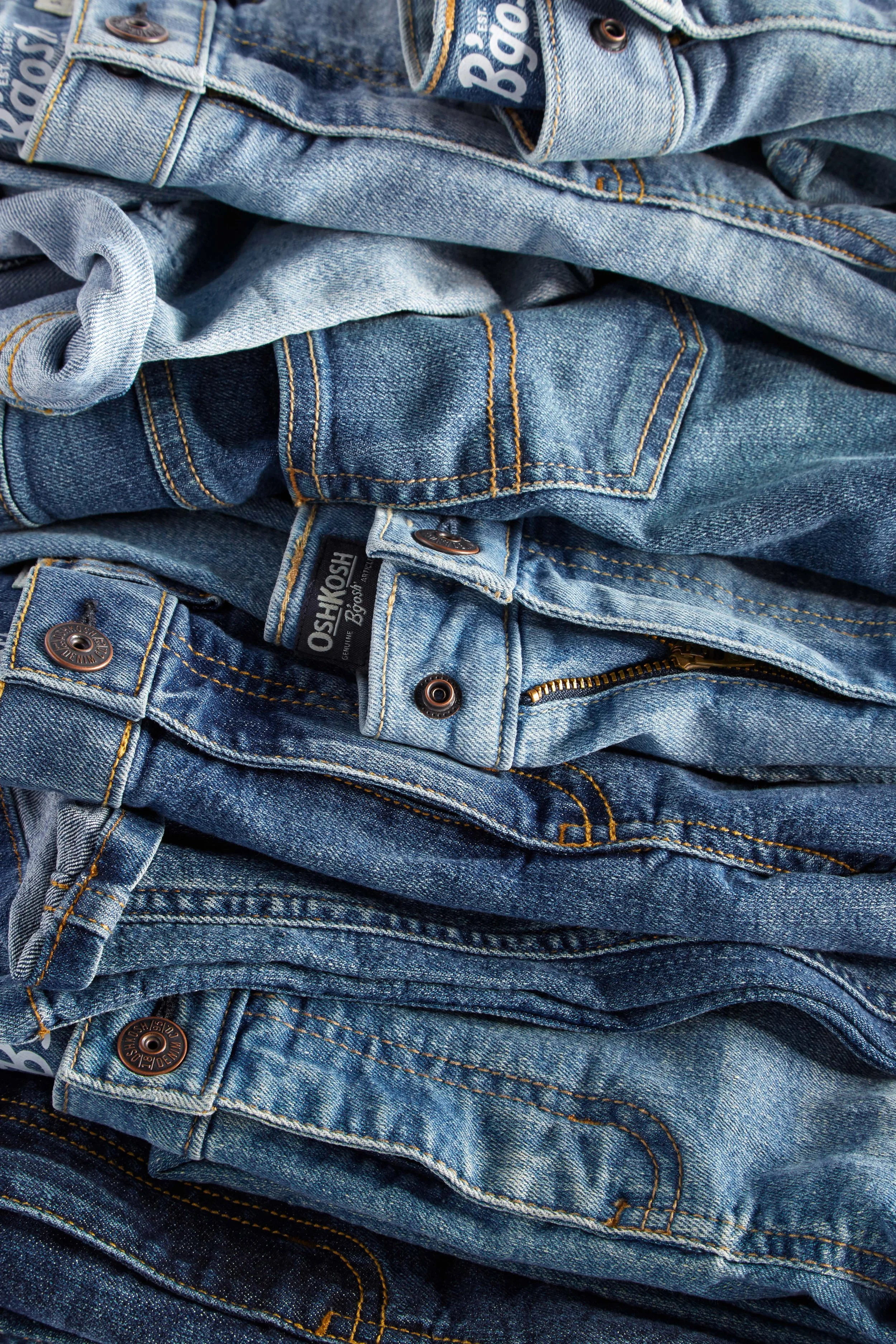 Stack of blue denim jeans with visible stitching, buttons, and zippers, arranged in layered piles.