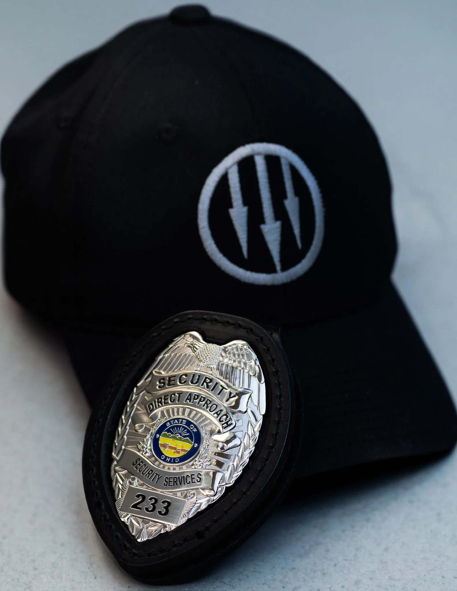 Close-up of a police badge embedded in a black wristband, with a smaller badge or badge-like object partially visible at the bottom, on a gray surface background.