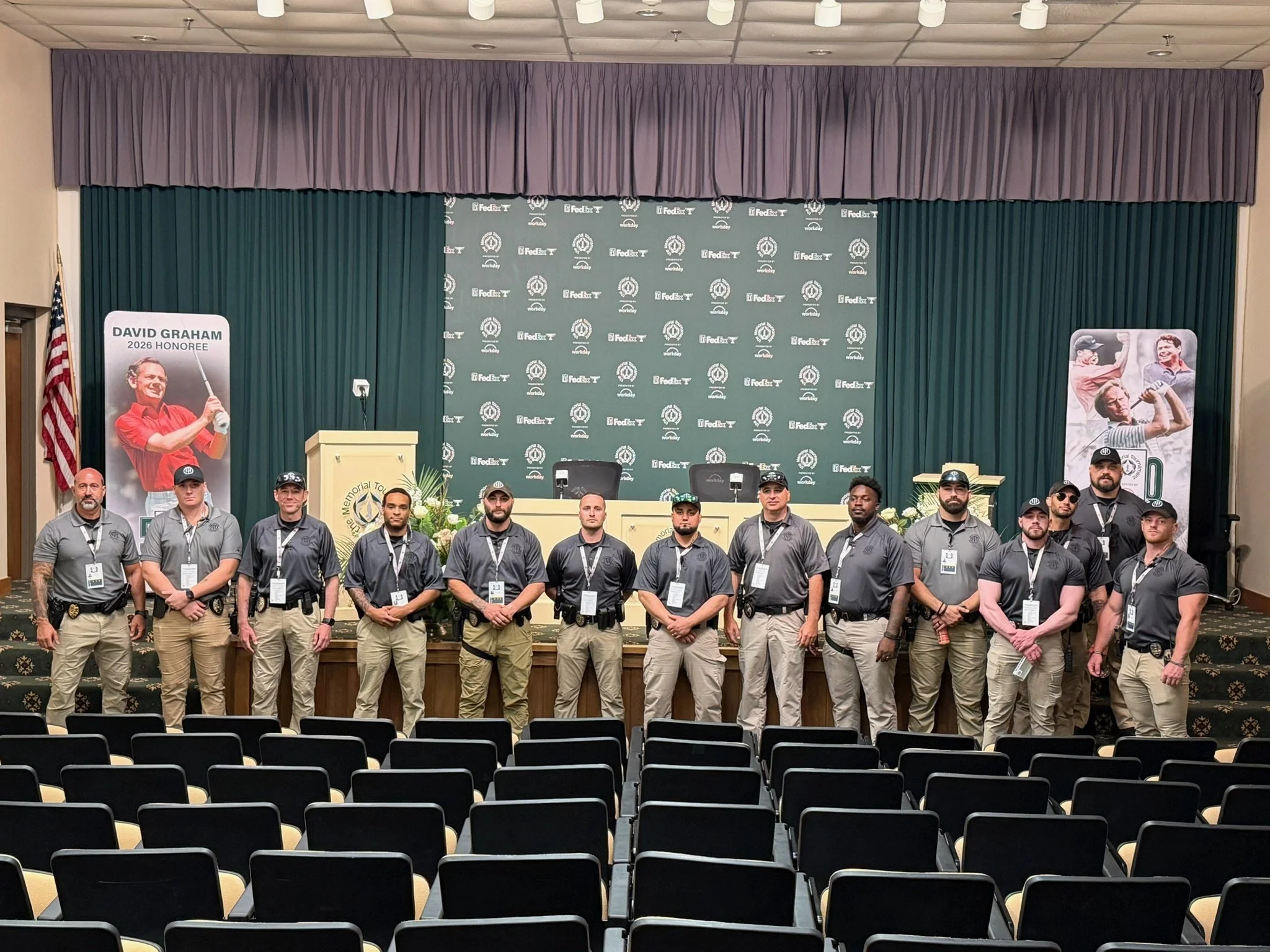 Group of people standing on a stage in front of a backdrop with logos, posing for a photo at an indoor event.