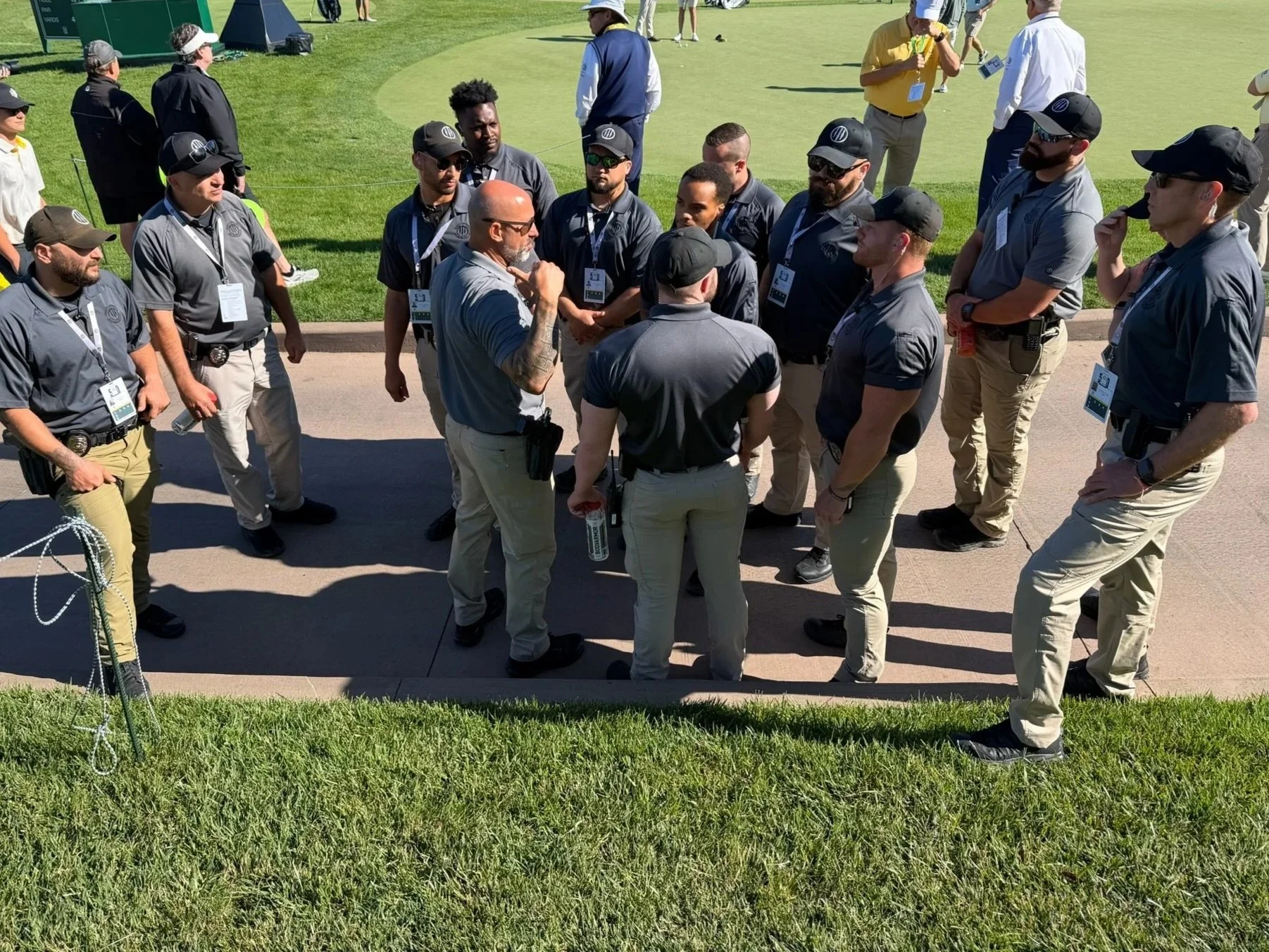 A group of security personnel and event staff gathered in a circle on a golf course, engaged in discussion.