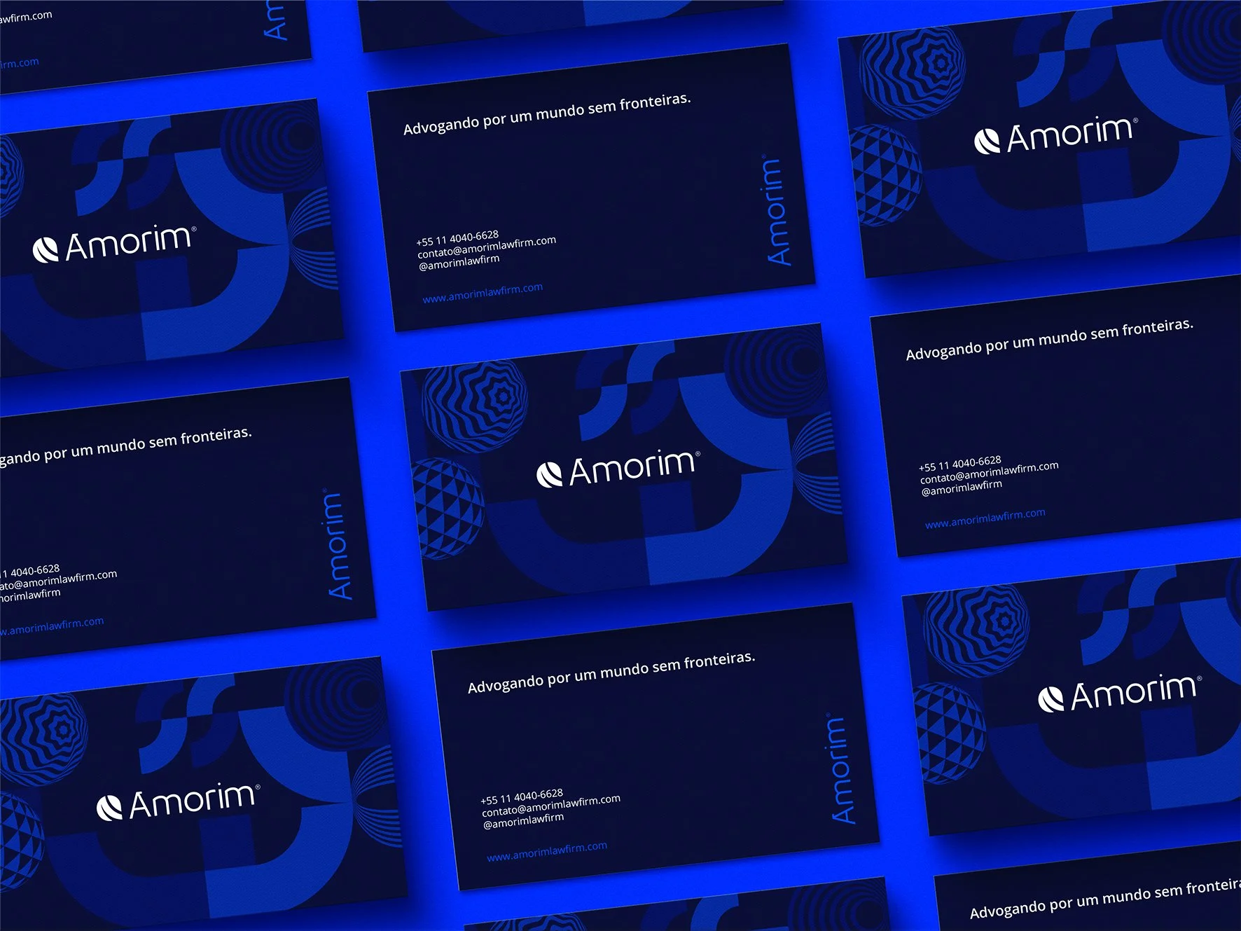 Cartões de visita da empresa Amorim com fundo azul escuro, apresentando o logo, o nome da empresa, o slogan 'Advogando por um mundo sem fronteiras', informações de contato e elementos gráficos geométricos