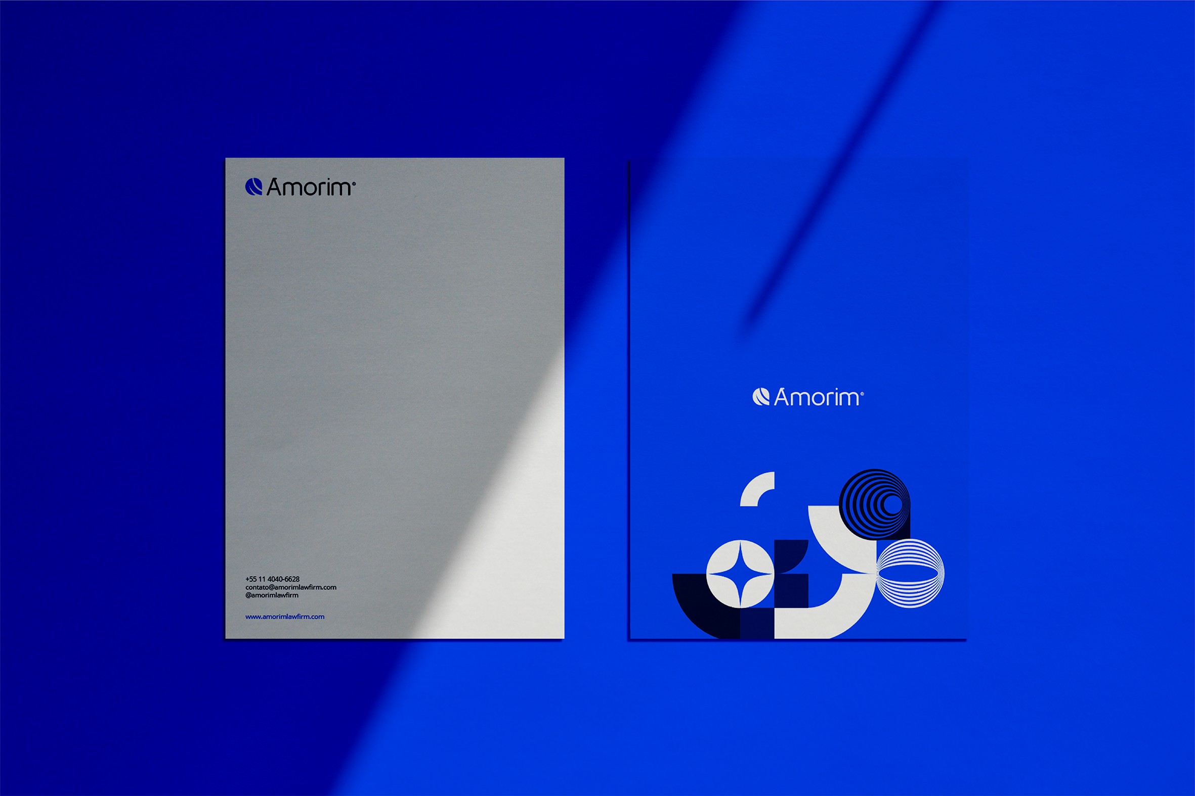 Folder branco com logotipo da Amorim e contatos na parte inferior, ao lado de uma placa azul com logotipo da Amorim e design geométrico.