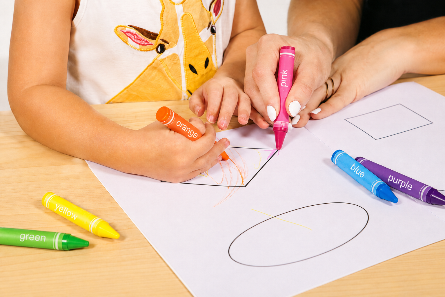 Criança e adulto usando marcadores de cores diferentes para colori e desenhar num papel. A criança veste uma camiseta com estampa de girafa.
