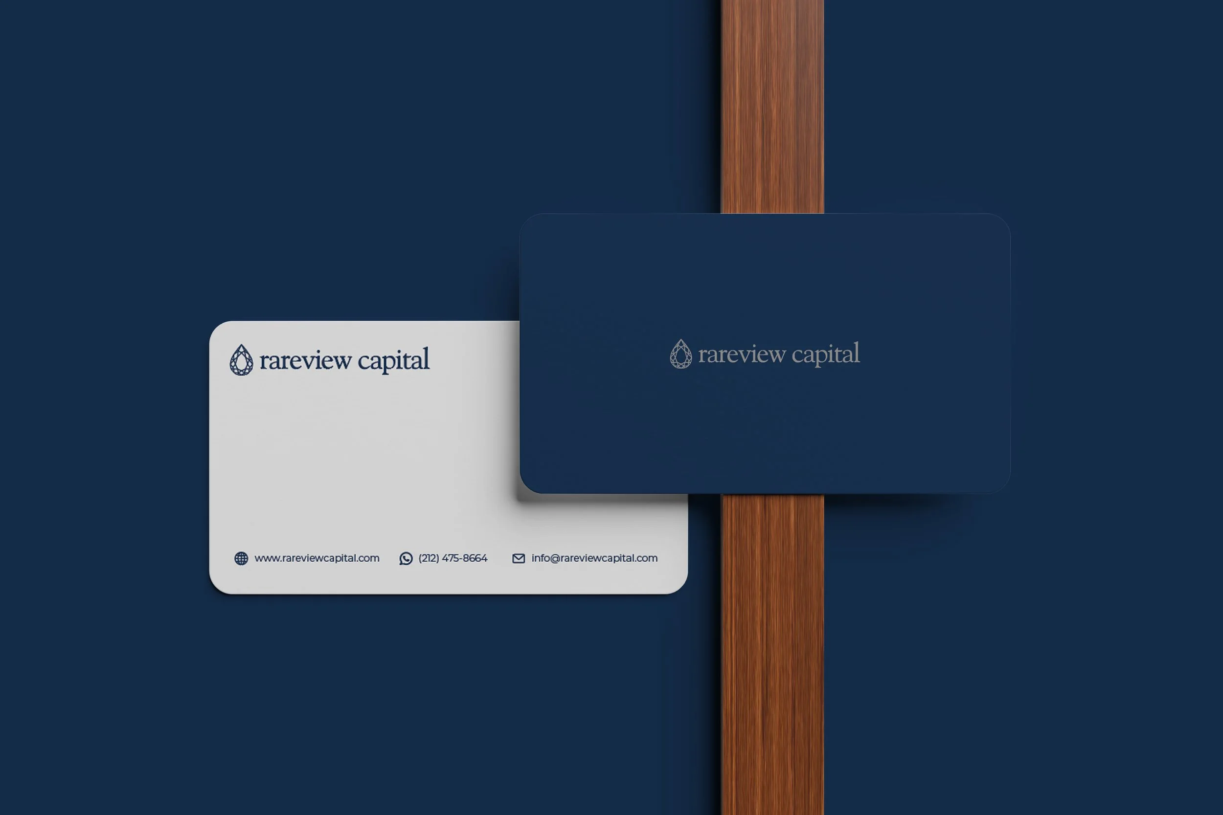 Cartões de visita com o logotipo da Rareview Capital, empresa de investimentos, com cores azul escuro e branco, sobre uma mesa de madeira.