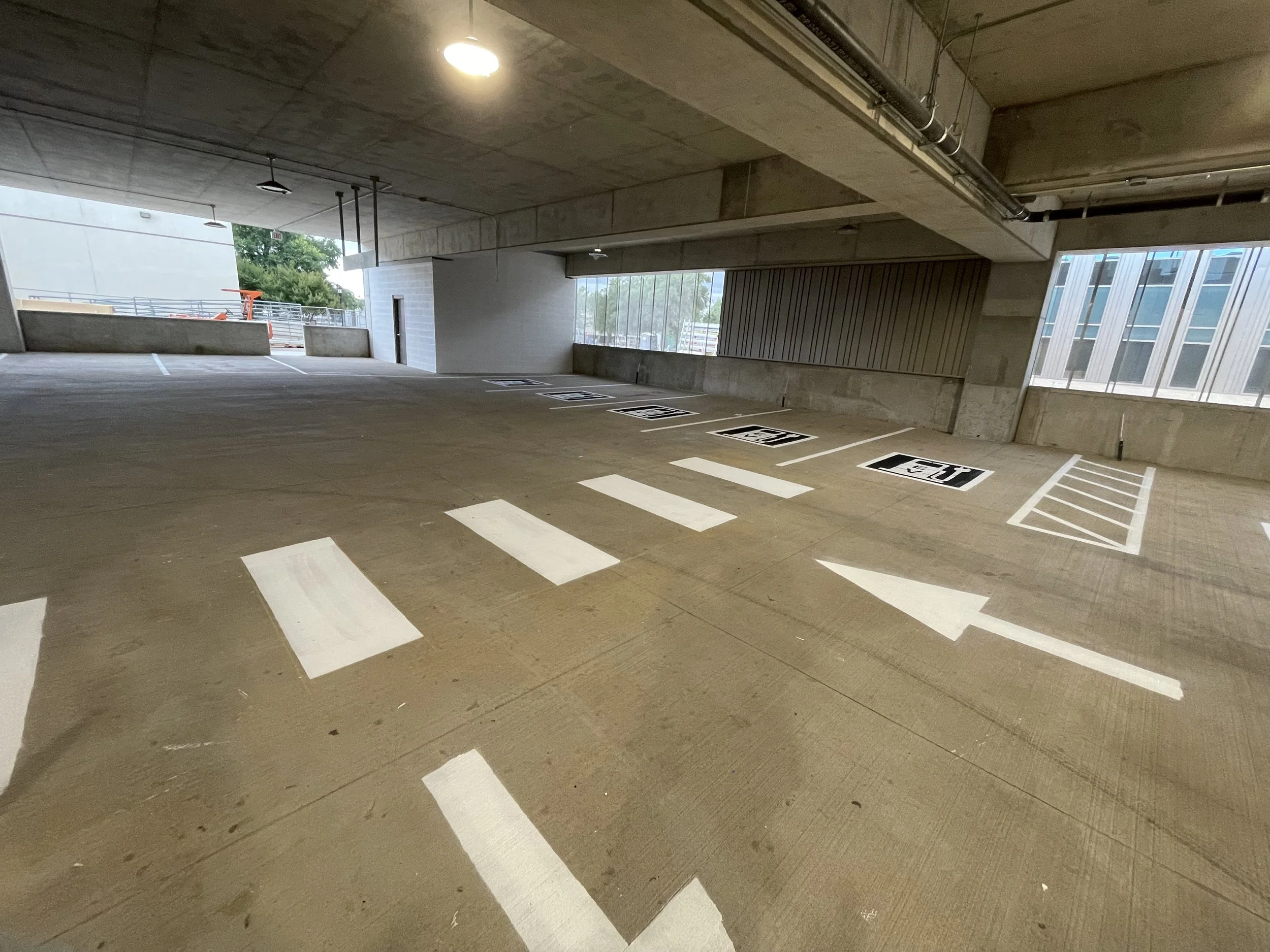 Empty parking garage with marked parking spaces, concrete walls, and large windows providing natural light.