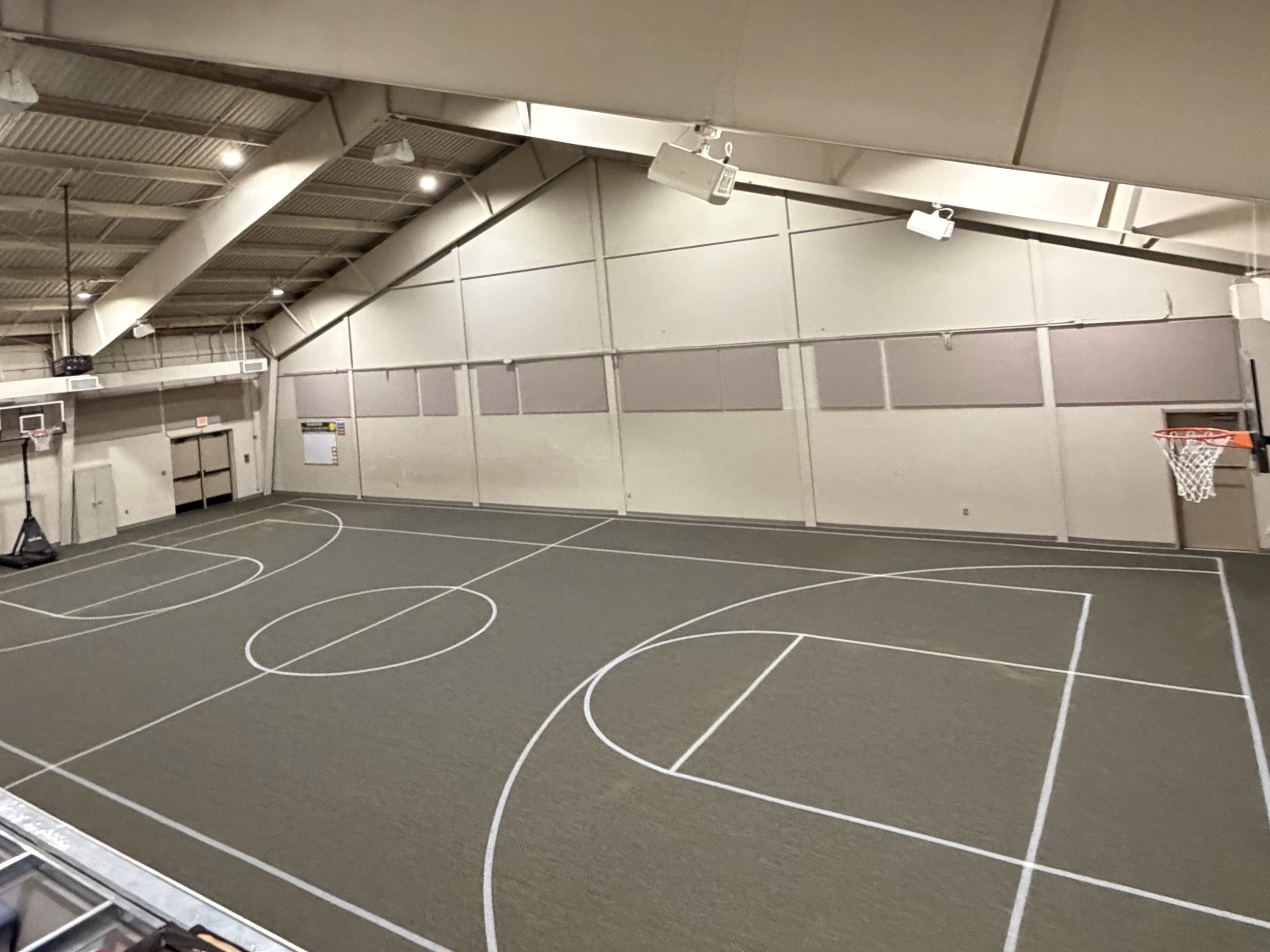 An indoor gymnasium with a basketball court, basketball hoops, and overhead lighting.