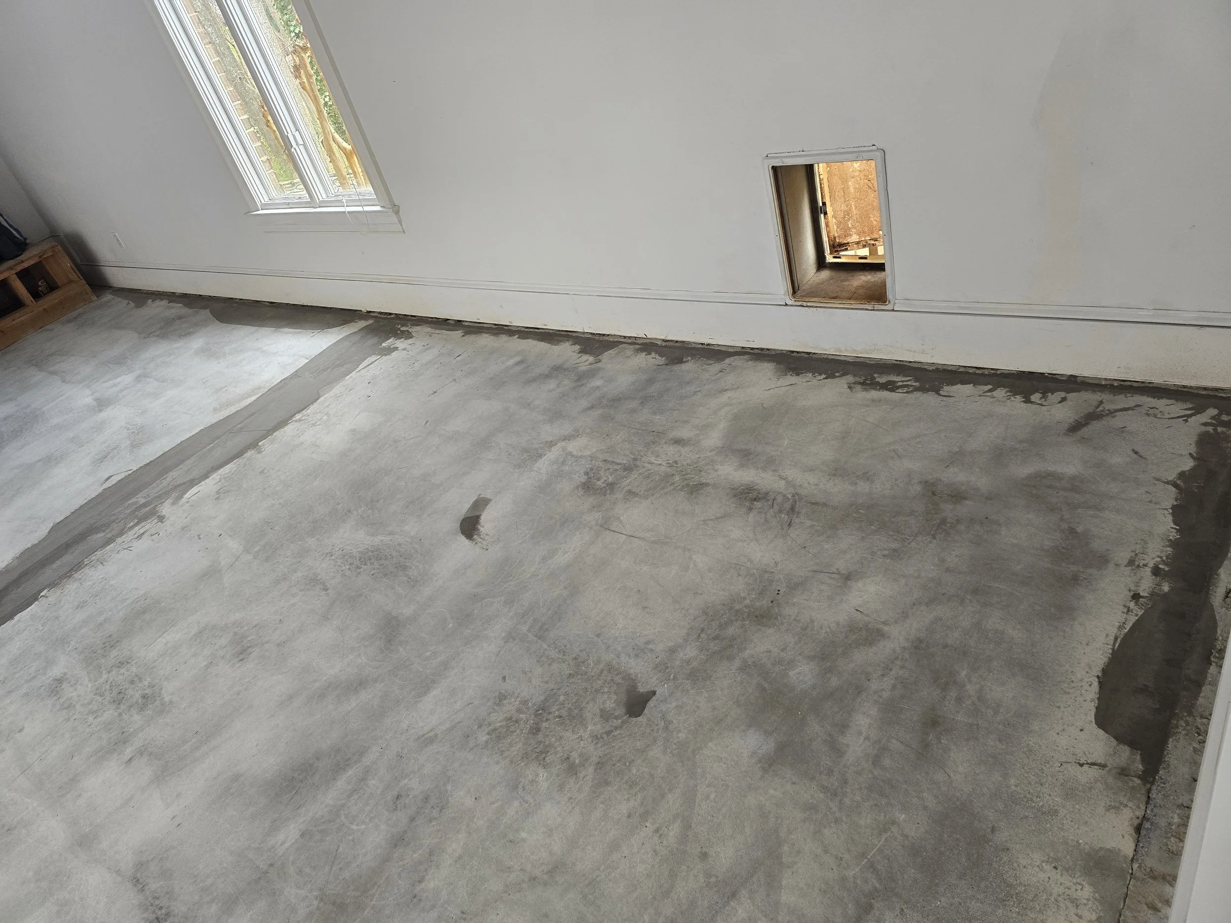 Empty room with a window and a small access door near the floor, showing a view of an outdoor area.