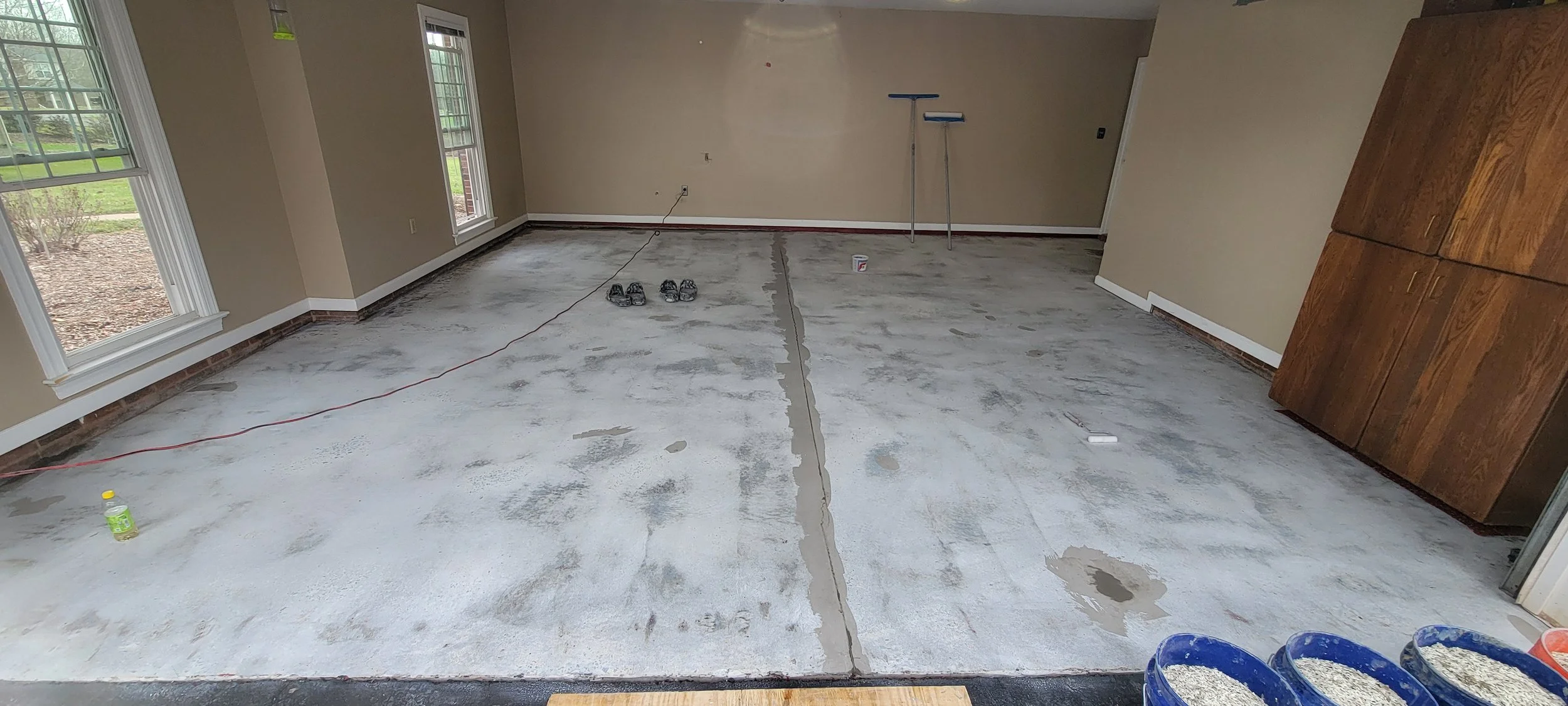 Interior of a room under renovation, with a concrete floor that is being prepared for new flooring, and tools and supplies scattered around.