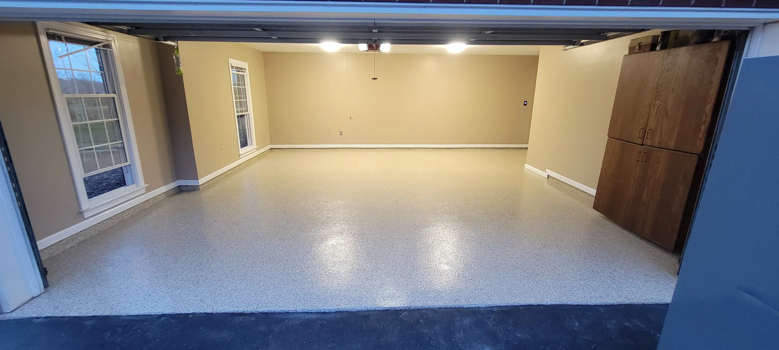 Empty garage with beige walls, three windows on the left, and a brown storage cabinet on the right side.