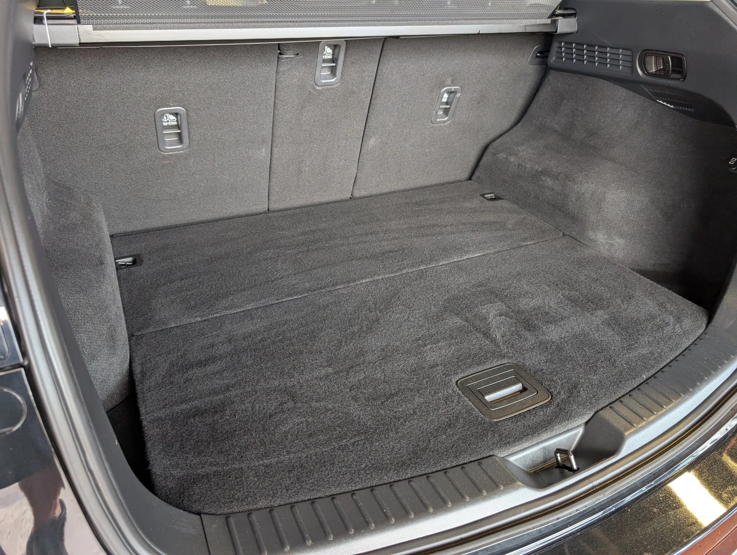 The trunk space of a car with a folded-down rear seat, showing a gray carpeted interior and metal latches for seat fold mechanisms.
