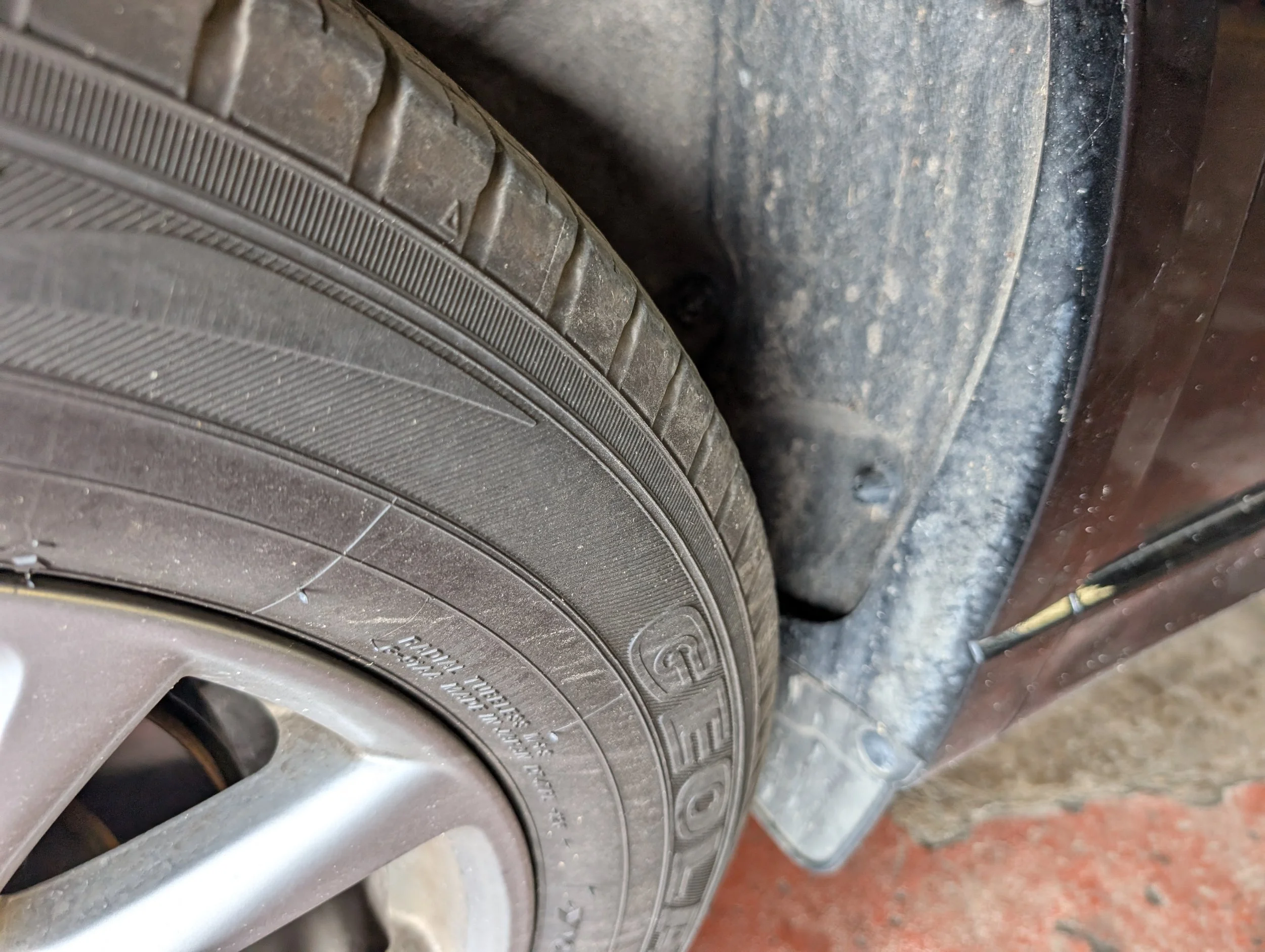 Close-up of a car tire and rim, with the tire mounted on a vehicle, showing the tread pattern and sidewall details.