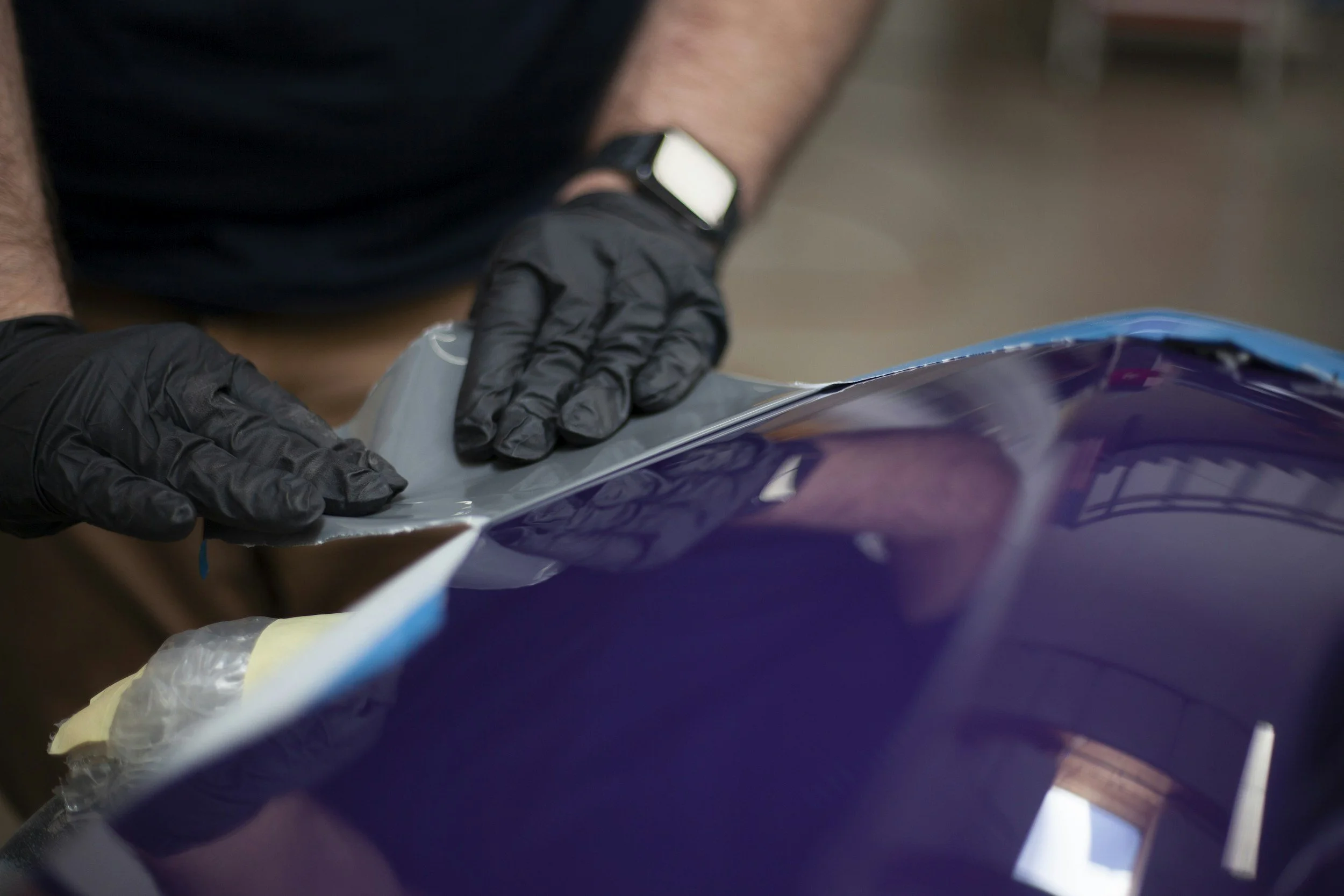 Person wearing black gloves handling a plastic sheet or film, with a watch visible on their wrist.