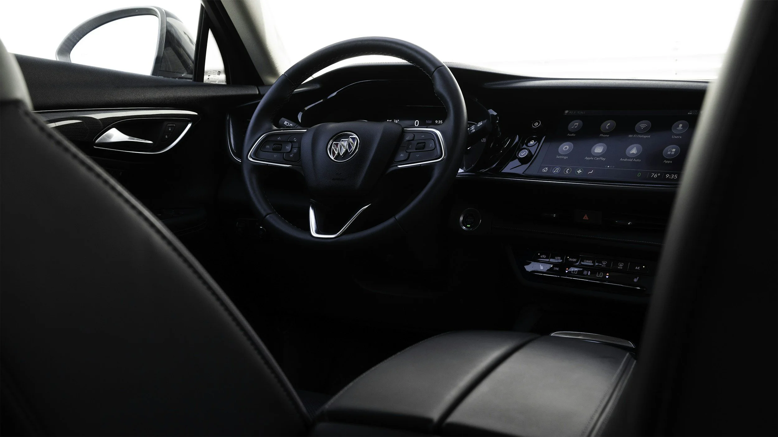 Interior view of a car dashboard displaying a steering wheel with a Buick logo, a digital instrument cluster, and an infotainment screen with icons for audio, phone, Wi-Fi hotspot, settings, and apps.