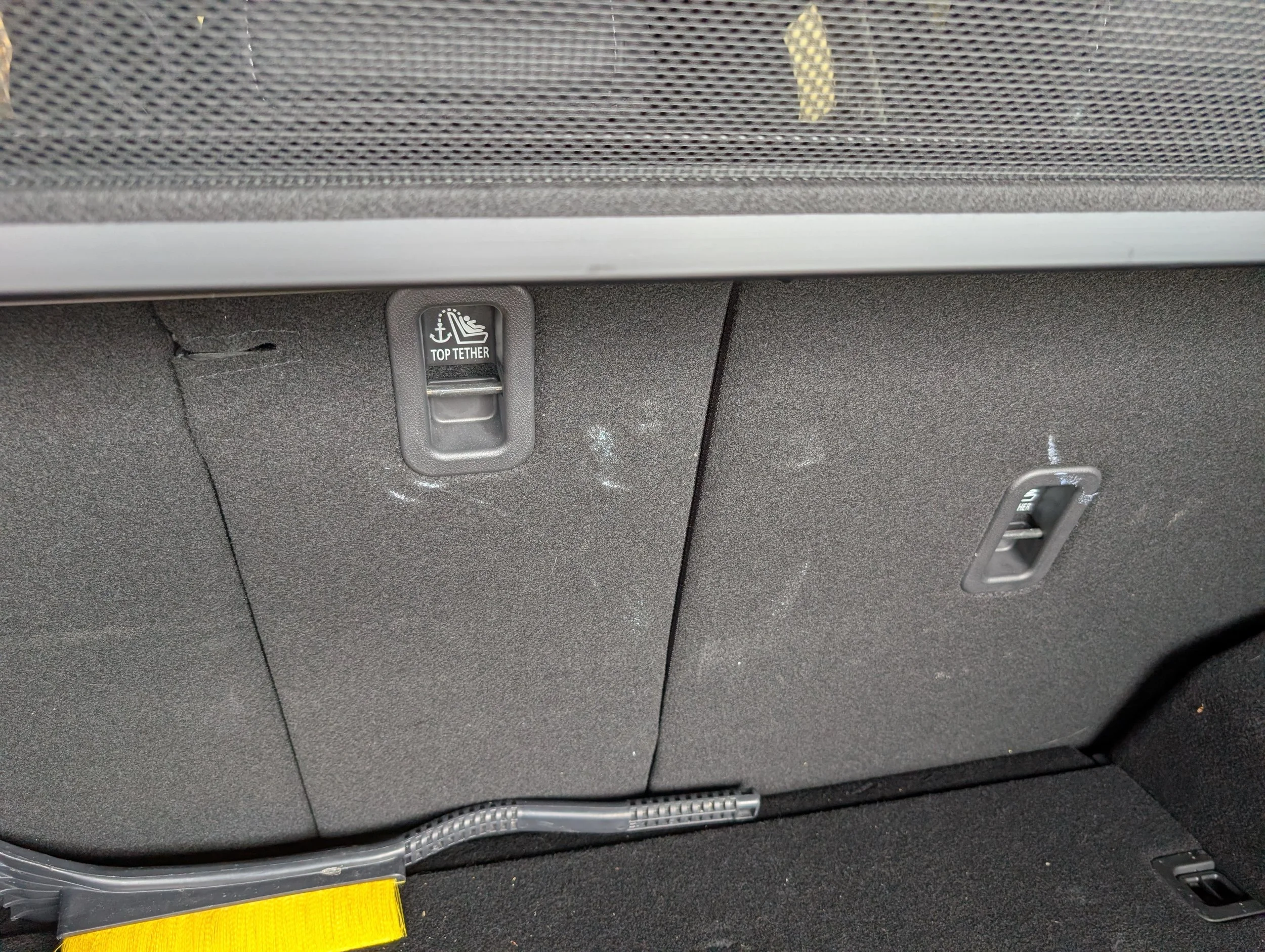 The interior of a vehicle showing the back of a seat with a net storage area, a toggle switch labeled 'Top Tether', and some visible wiring along the bottom.