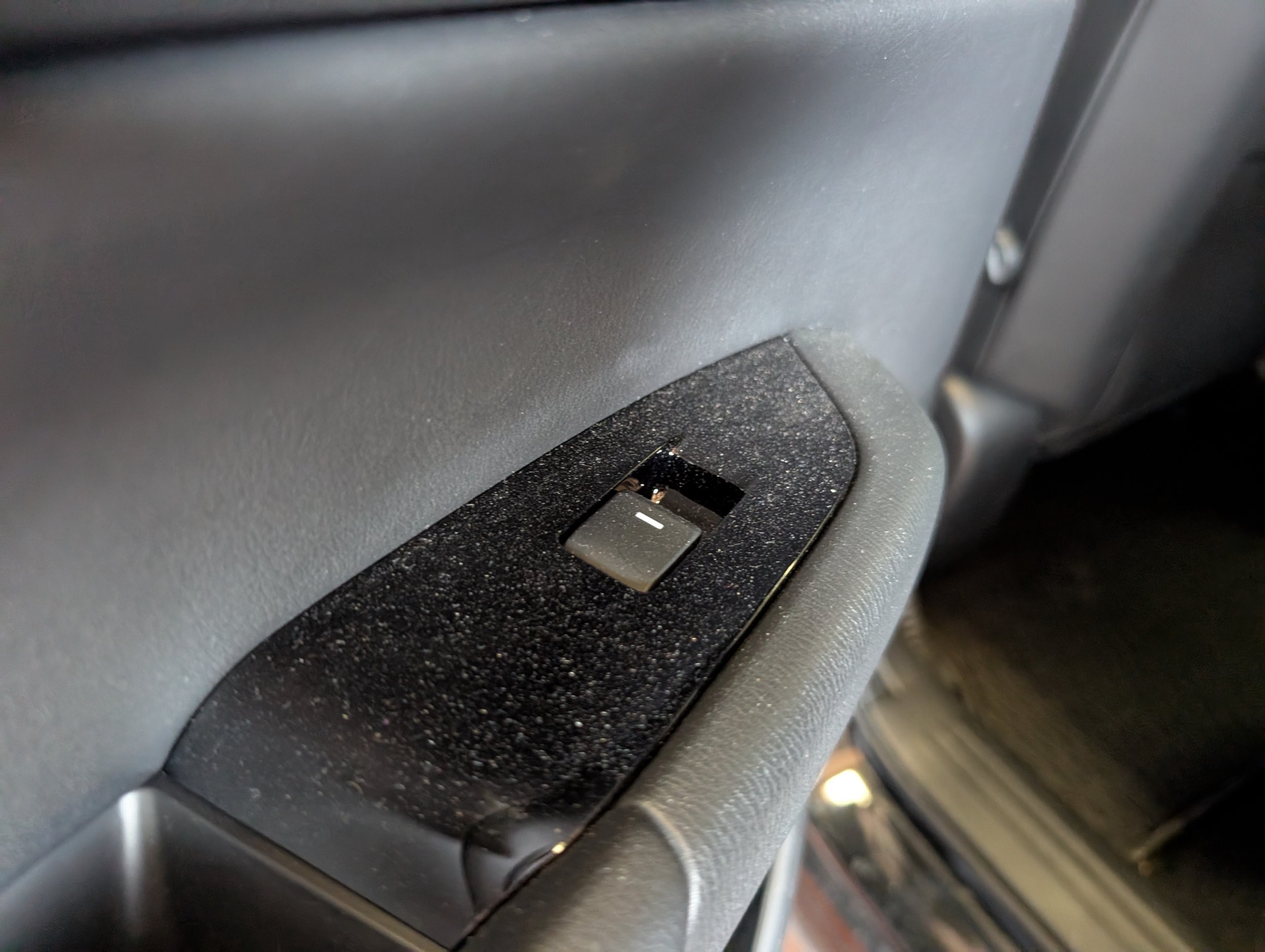 Close-up of a car's interior dashboard showing a black button with a white horizontal line, located near a textured surface and a metallic component.
