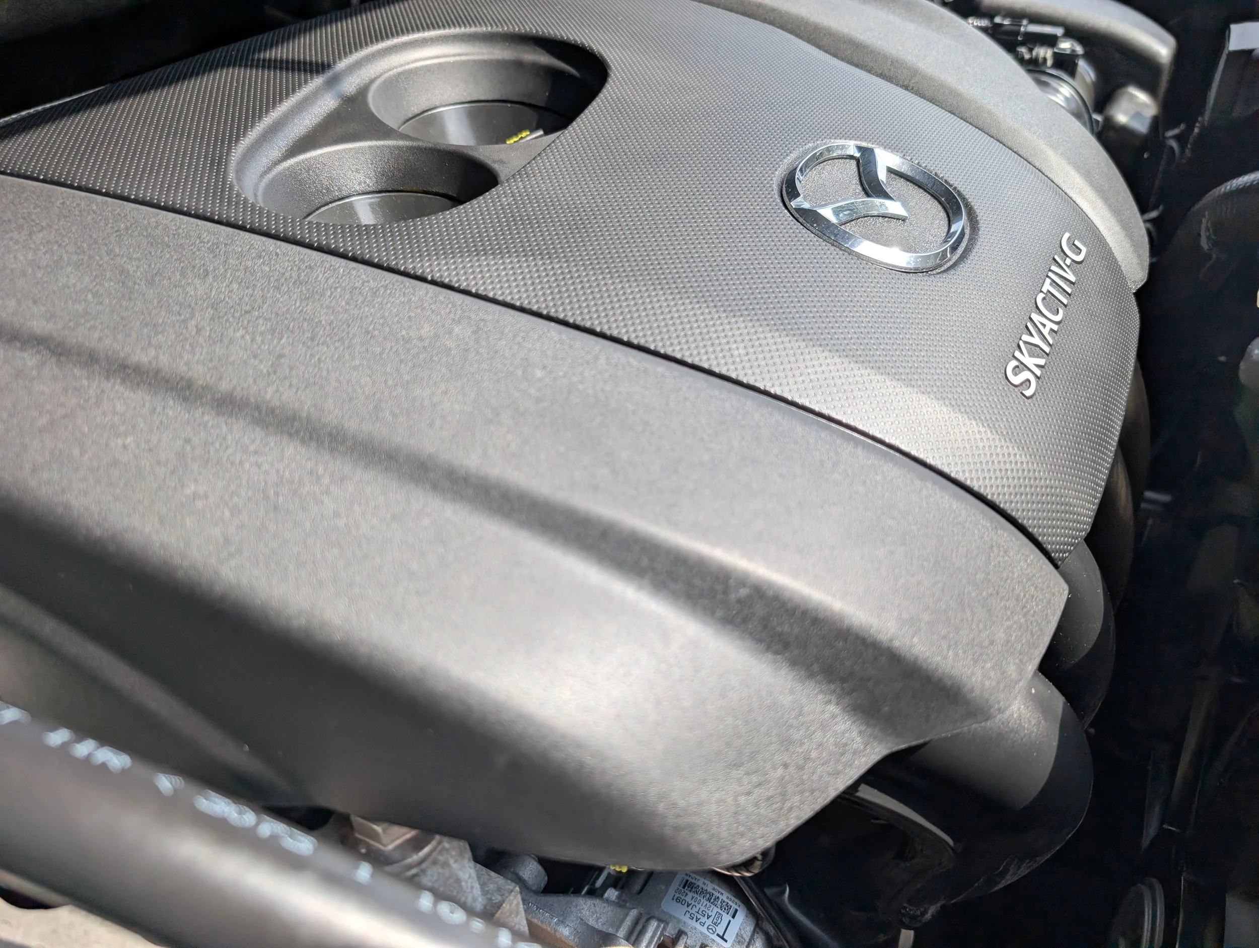 Close-up of a car engine cover with Mazda logo and the word 'SKYACTIV' printed on it.