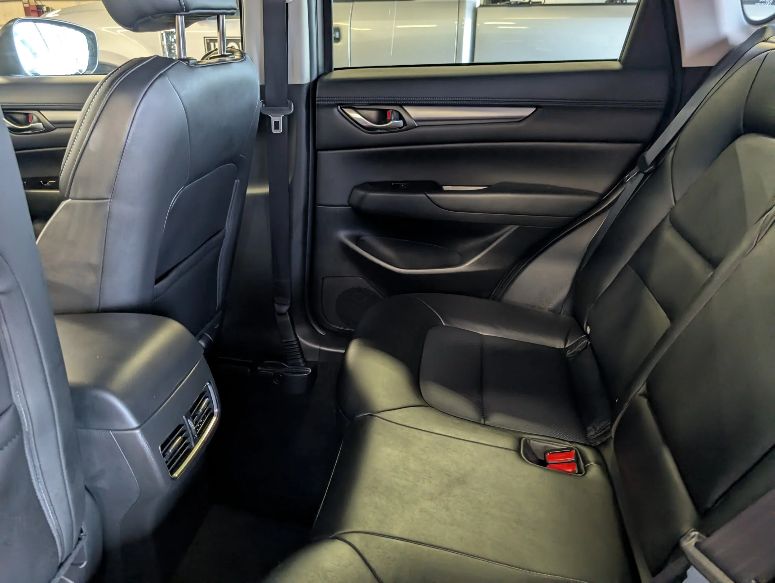 The interior of a modern car showing the backseat area with black leather seats, rear air vents, and partially visible front seats and window.