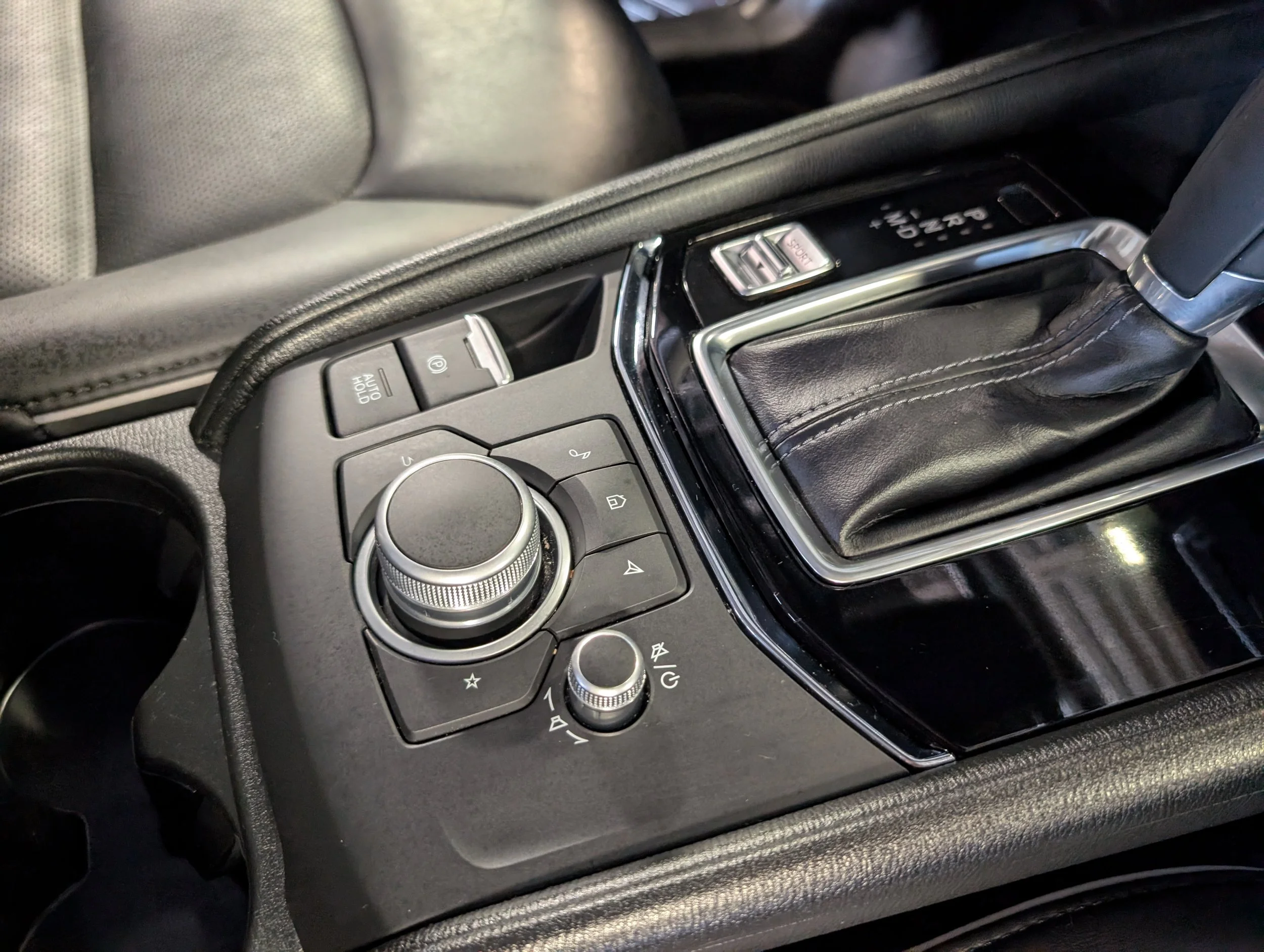 Close-up of a car’s center console featuring controls, a gear shift, and a black leather armrest.