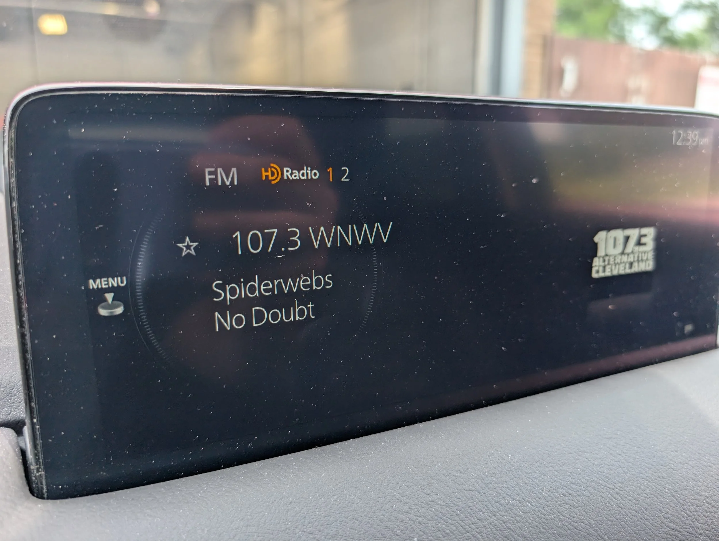 Car radio display showing station 107.3 WNW and song title 'Spiderwebs' by No Doubt, with additional station logo and time 12:39.