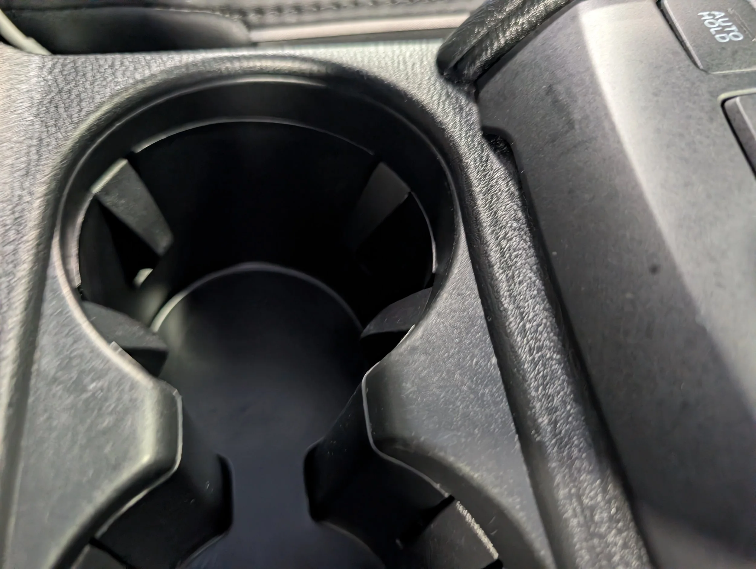 Close-up of a car's cup holder and dashboard area, with part of the gear shift and vehicle controls visible.