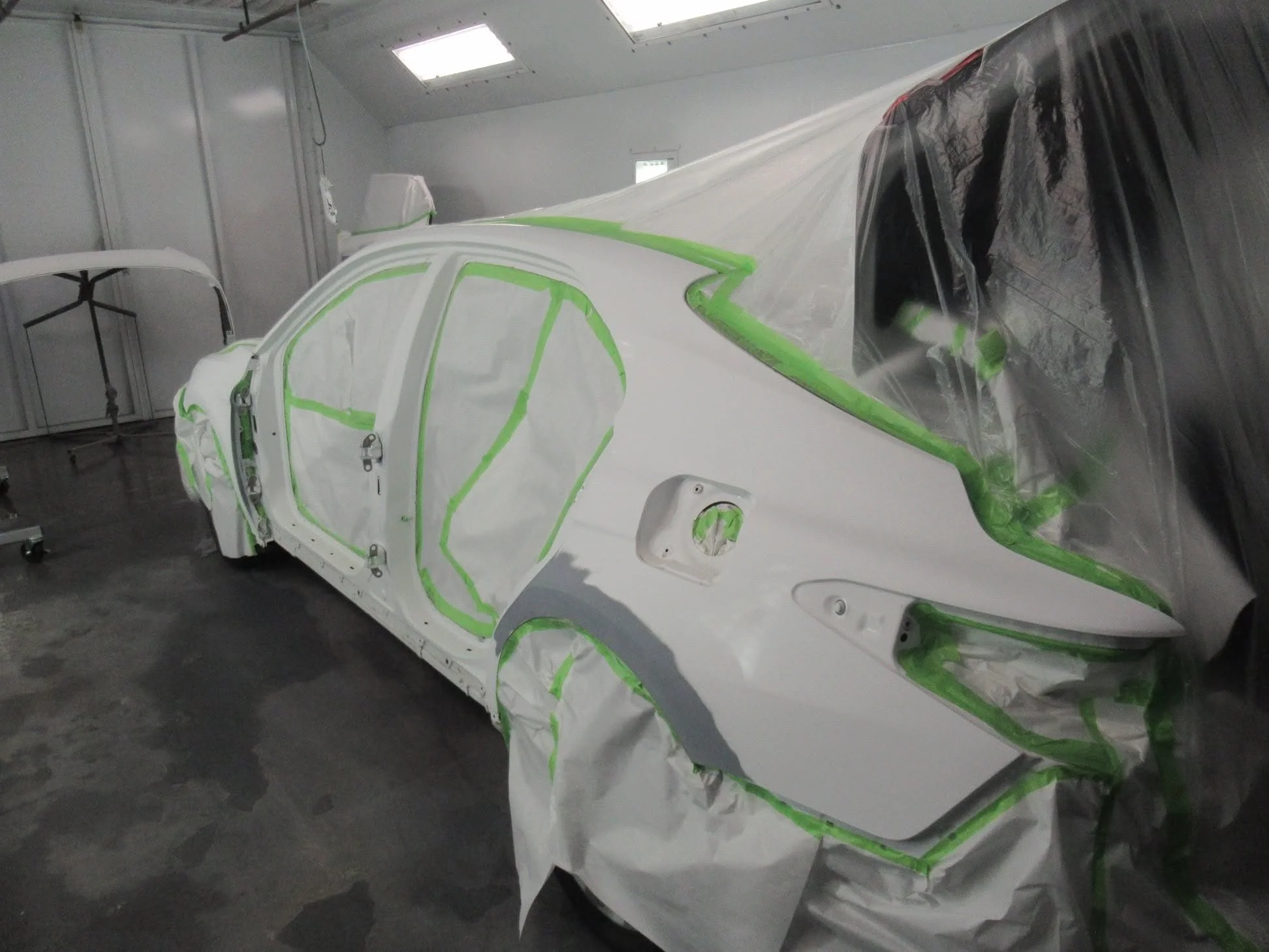 Car body parts covered with masking tape and plastic sheeting, likely in a paint booth for painting or repair.