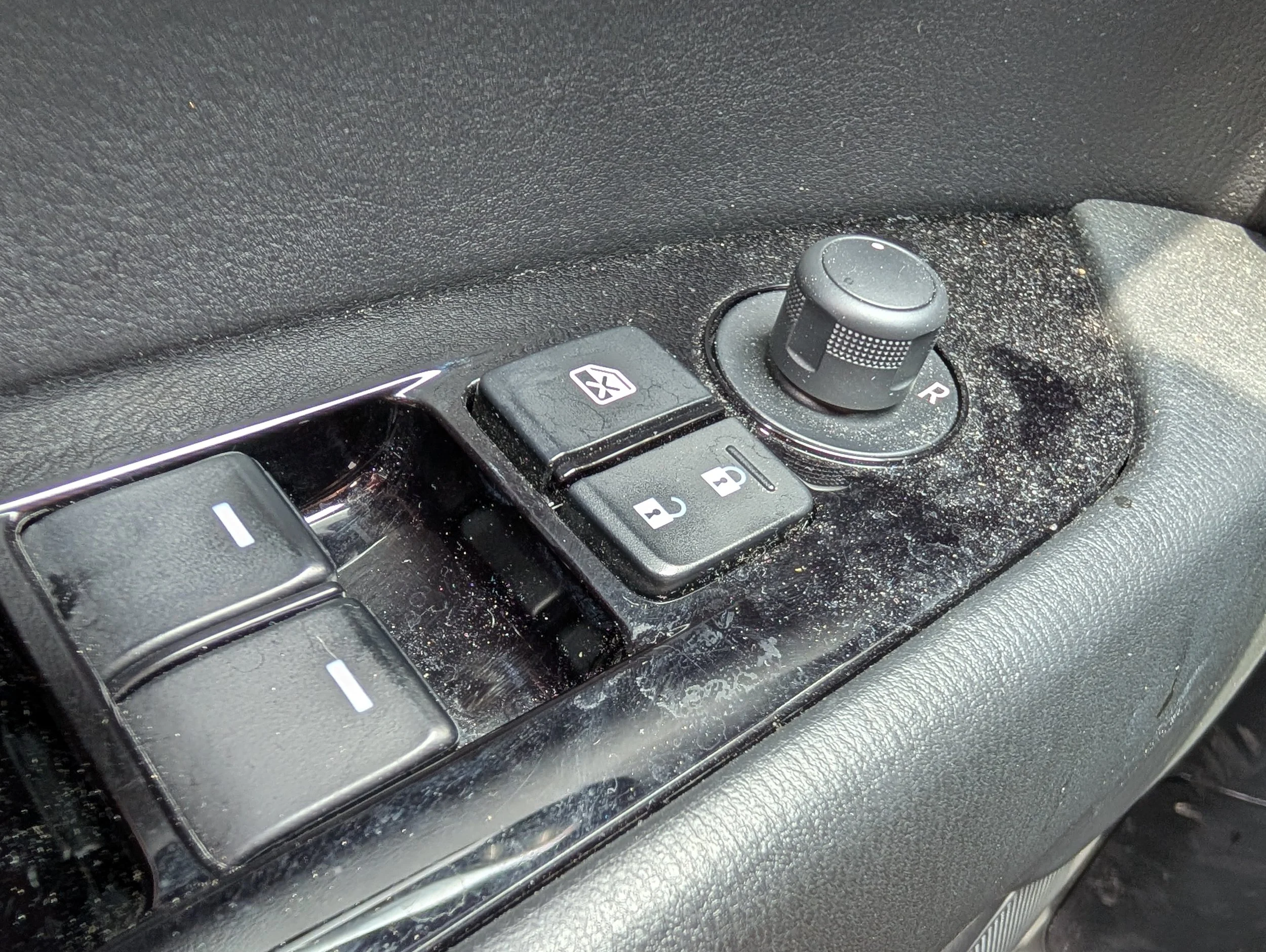 Close-up of a car's interior dashboard showing a rotary knob, buttons, and textured black surface.