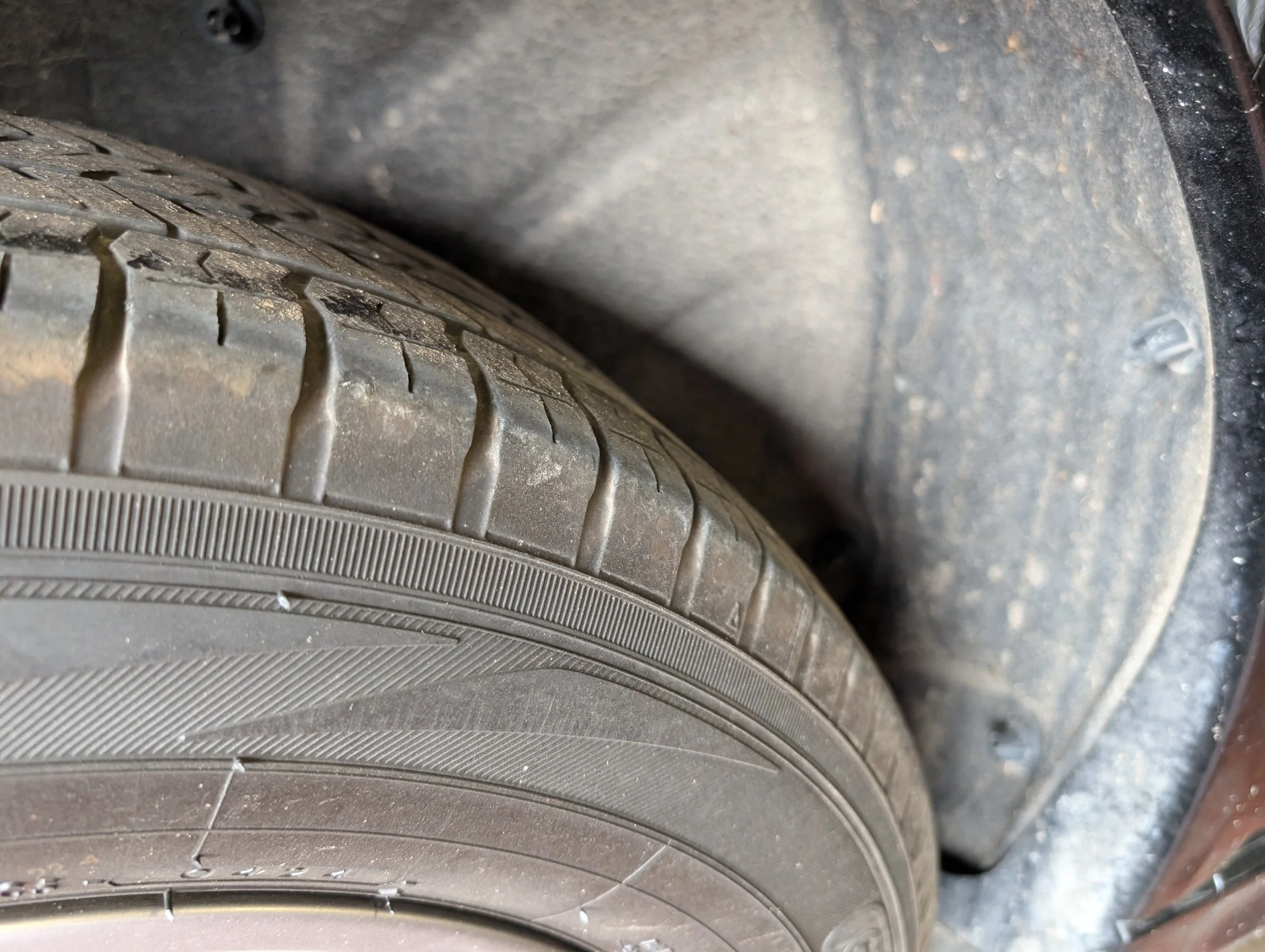 Close-up view of a car tire and wheel well, with the tire showing tread pattern and some dirt on its surface.