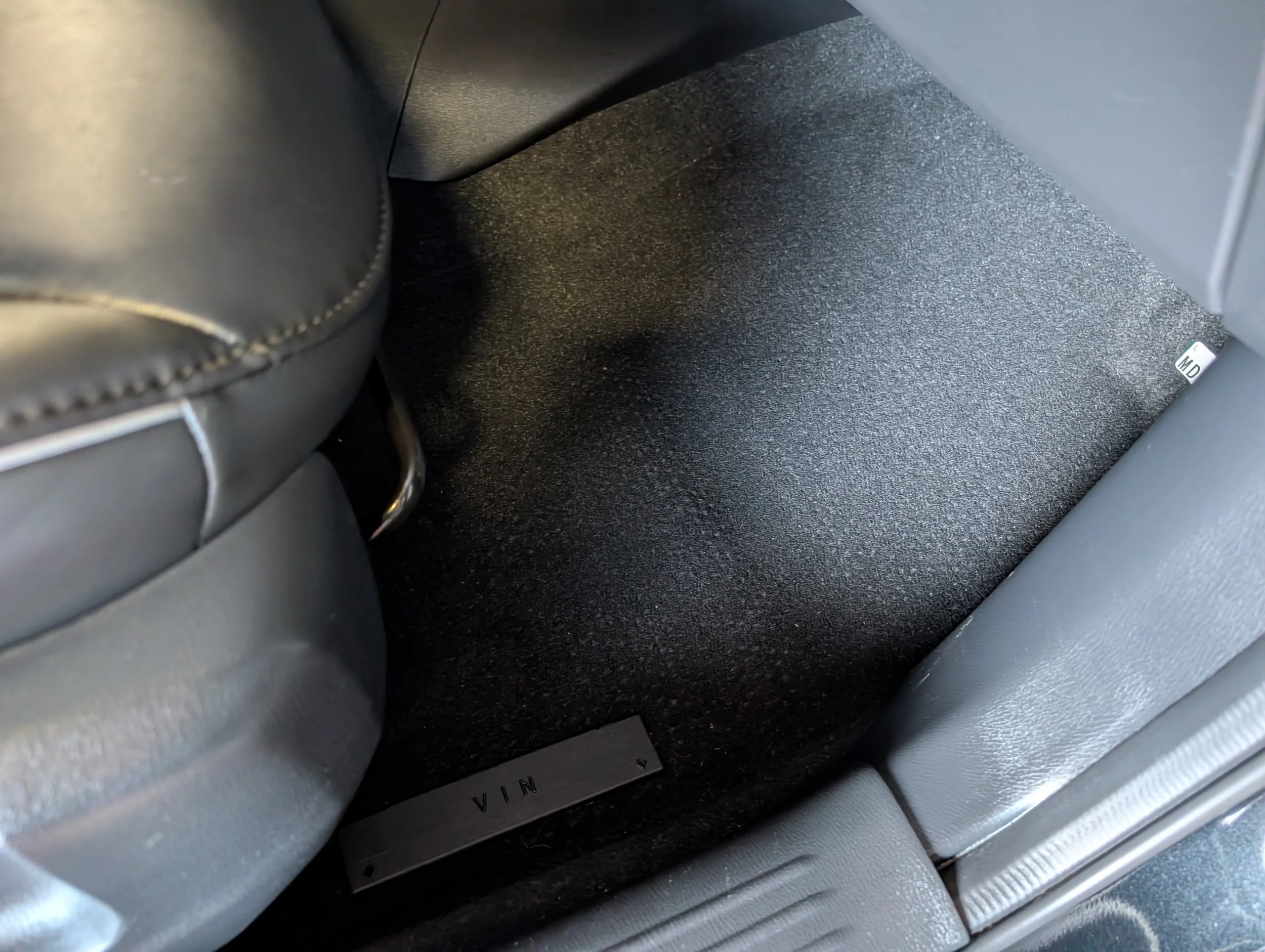 Close-up of the interior of a vehicle, showing parts of the seat, the floor, and a metallic plate with the word 'VIRGIN' engraved on it.