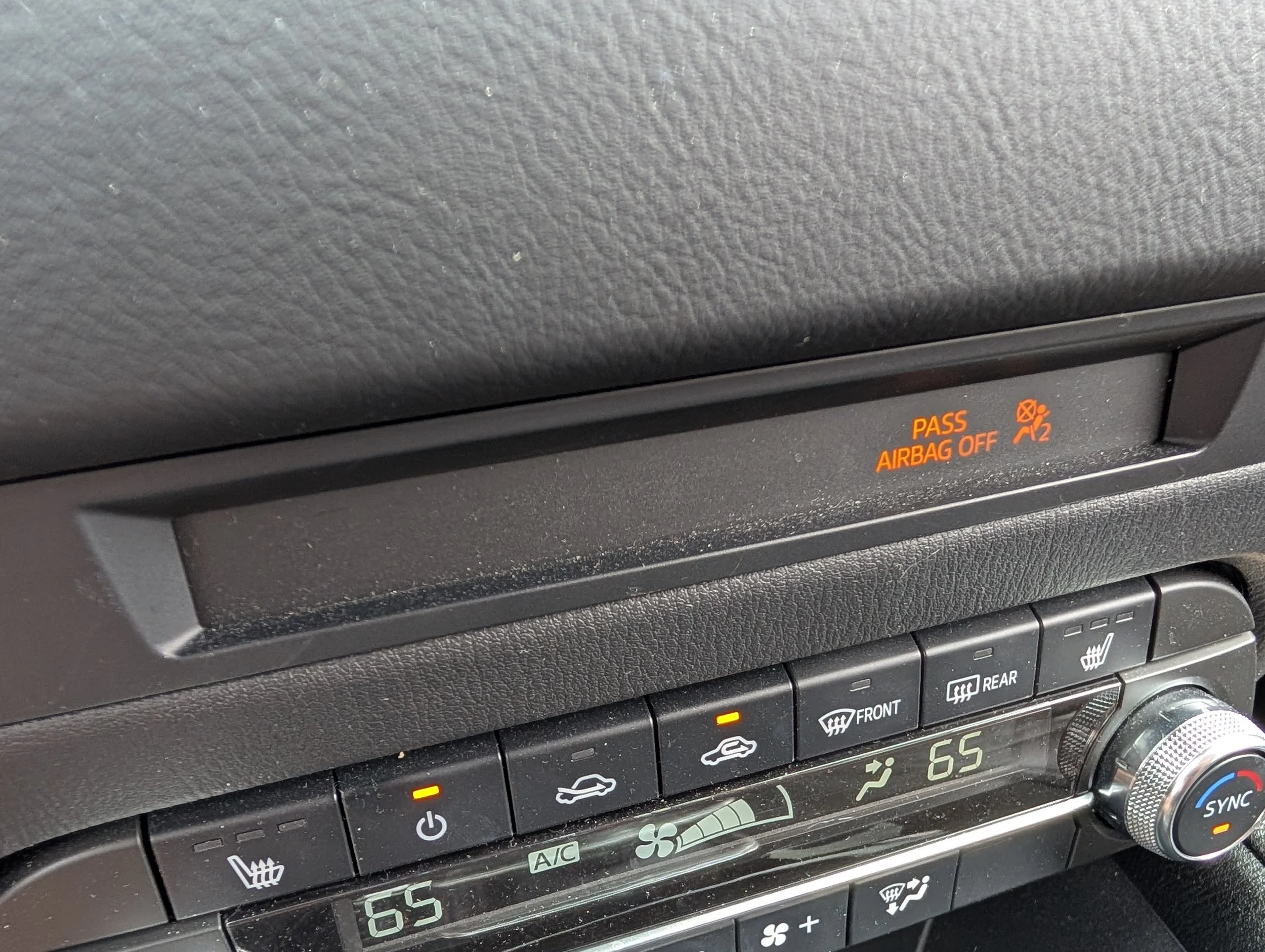 Car dashboard showing climate control buttons, digital display, and indicator lights, including a pass airbag off message.