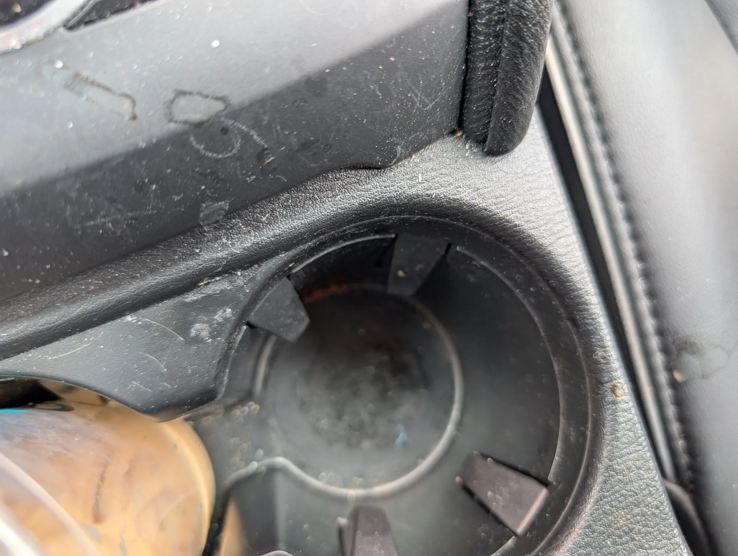 Close-up photo of a car's interior, showing part of the dashboard, cup holder, and a coffee mug with a brownish liquid.