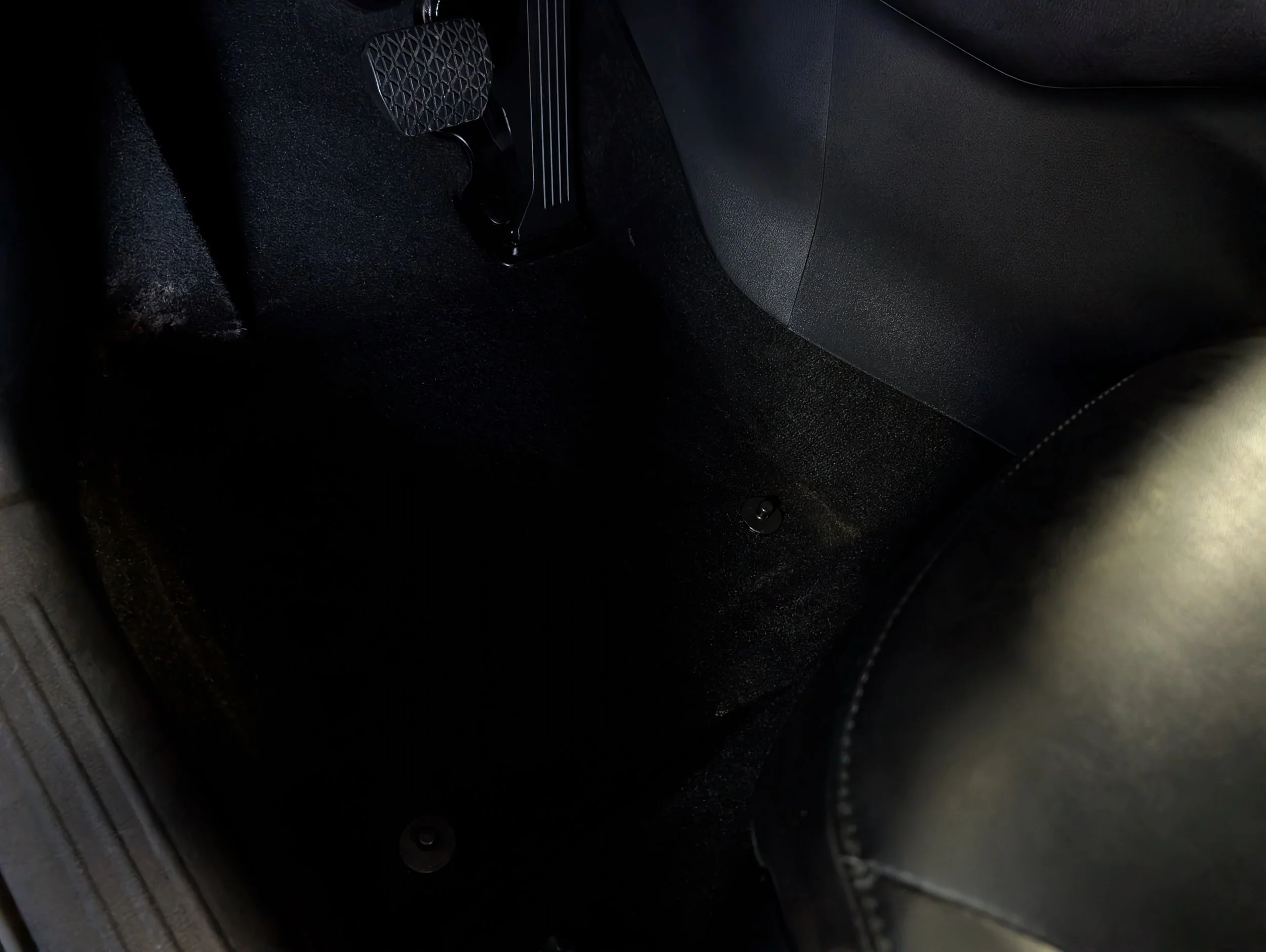 Close-up view of the foot pedals inside a car, including the accelerator pedal and brake pedal, on a black carpeted car floor.