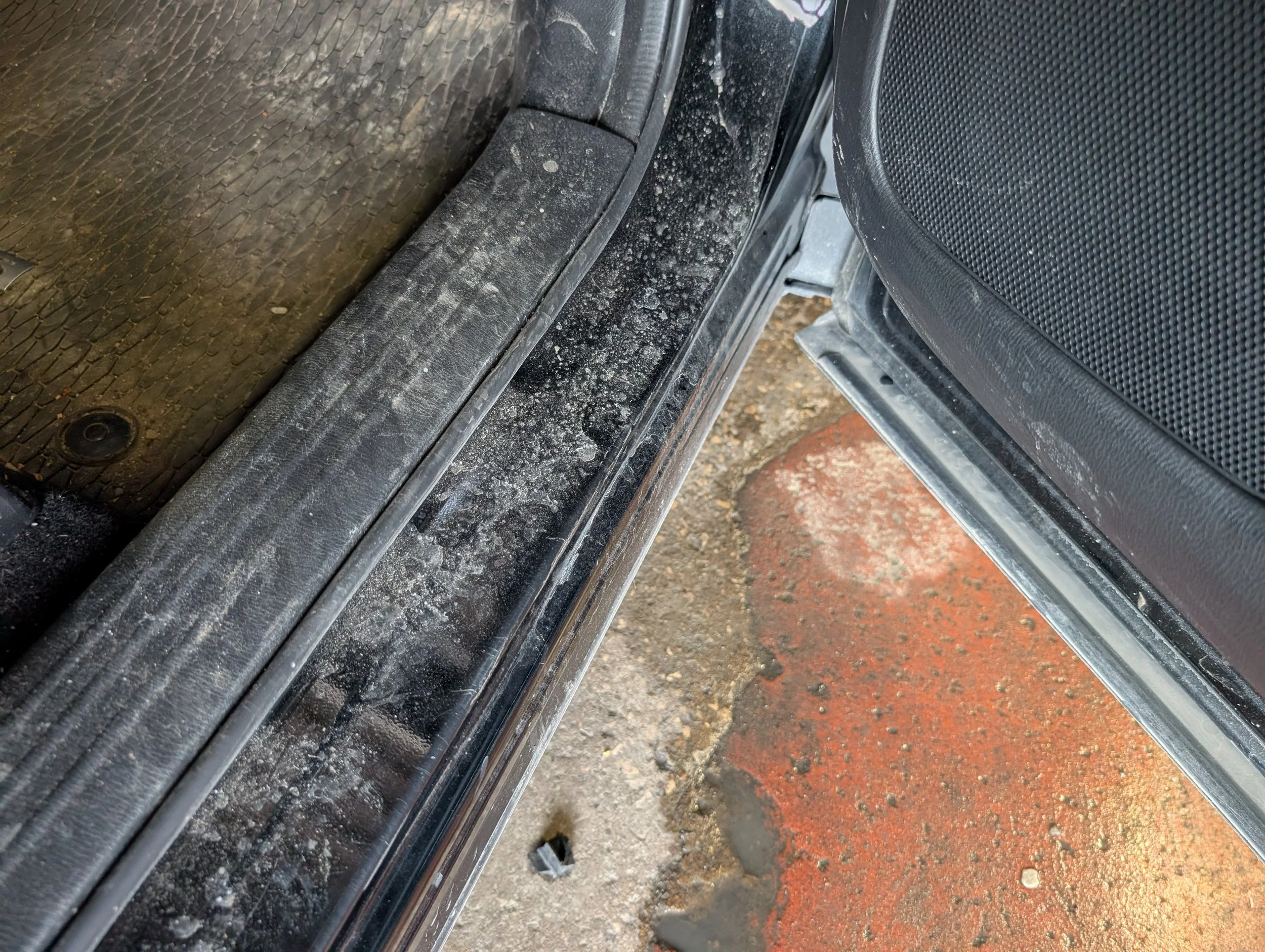 Close-up of a dirty black rubber door seal on a car, with visible dust and dirt, next to a textured black car interior door panel.