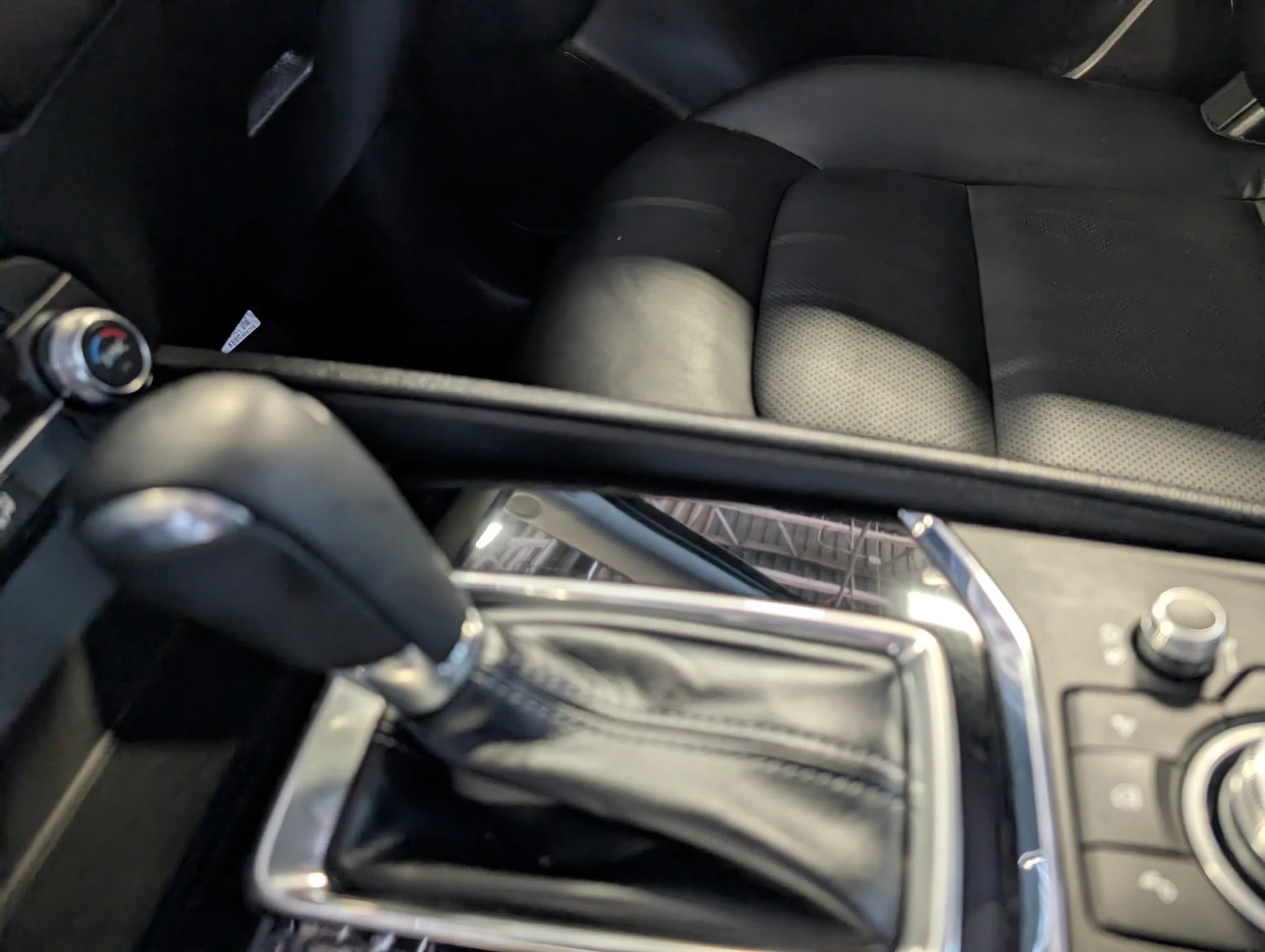 Interior of a car showing the driver and passenger seats, center console, gear shift, and part of the dashboard, with the seats being black and the dashboard having control knobs.