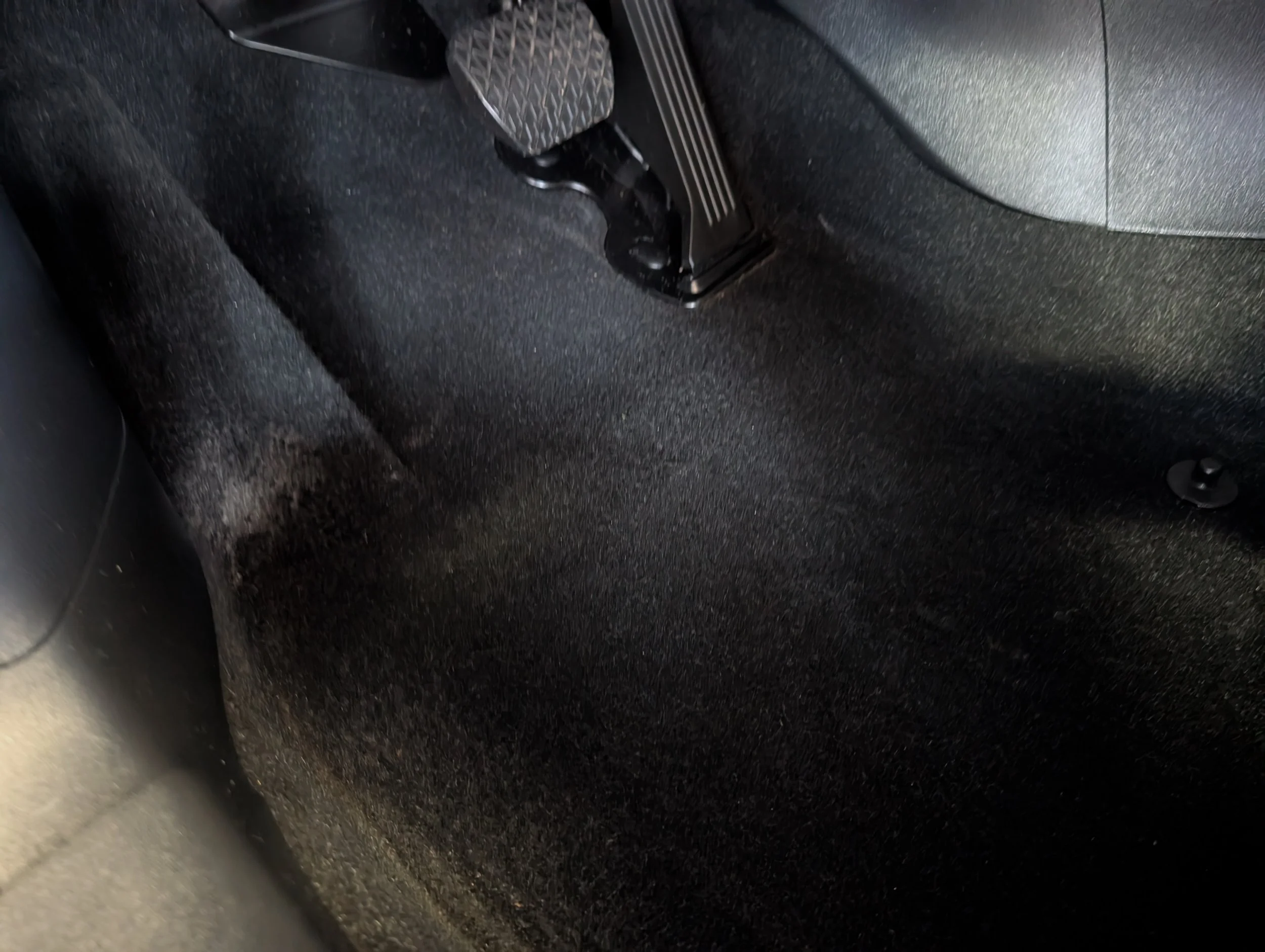 Close-up of car interior showing the accelerator pedal, brake pedal, and floor mat.