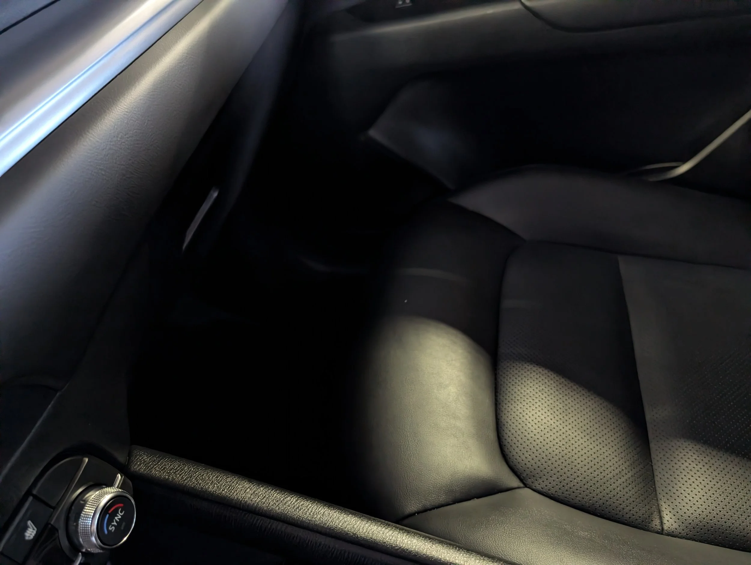 Close-up interior shot of a car dashboard and front seats, featuring a temperature control dial, a mix of smooth black plastic and textured materials, and a perforated seat surface.