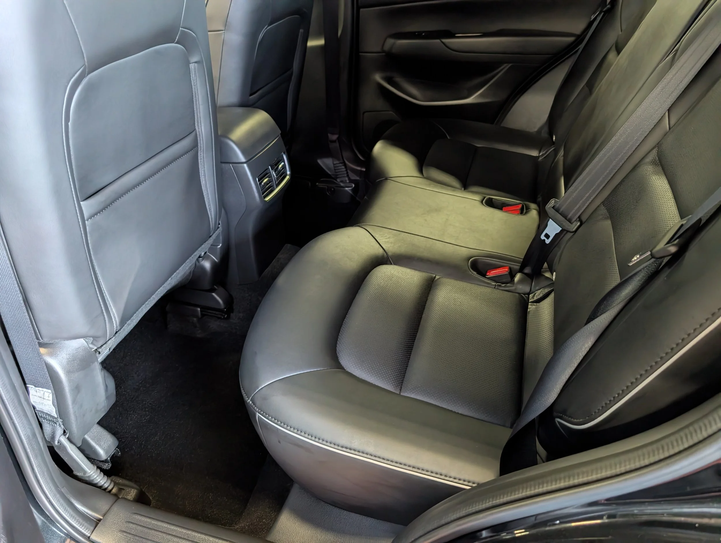 The backseat area of a car, showing gray leather seats and a black interior, with rear air vents on the back of the front seats.