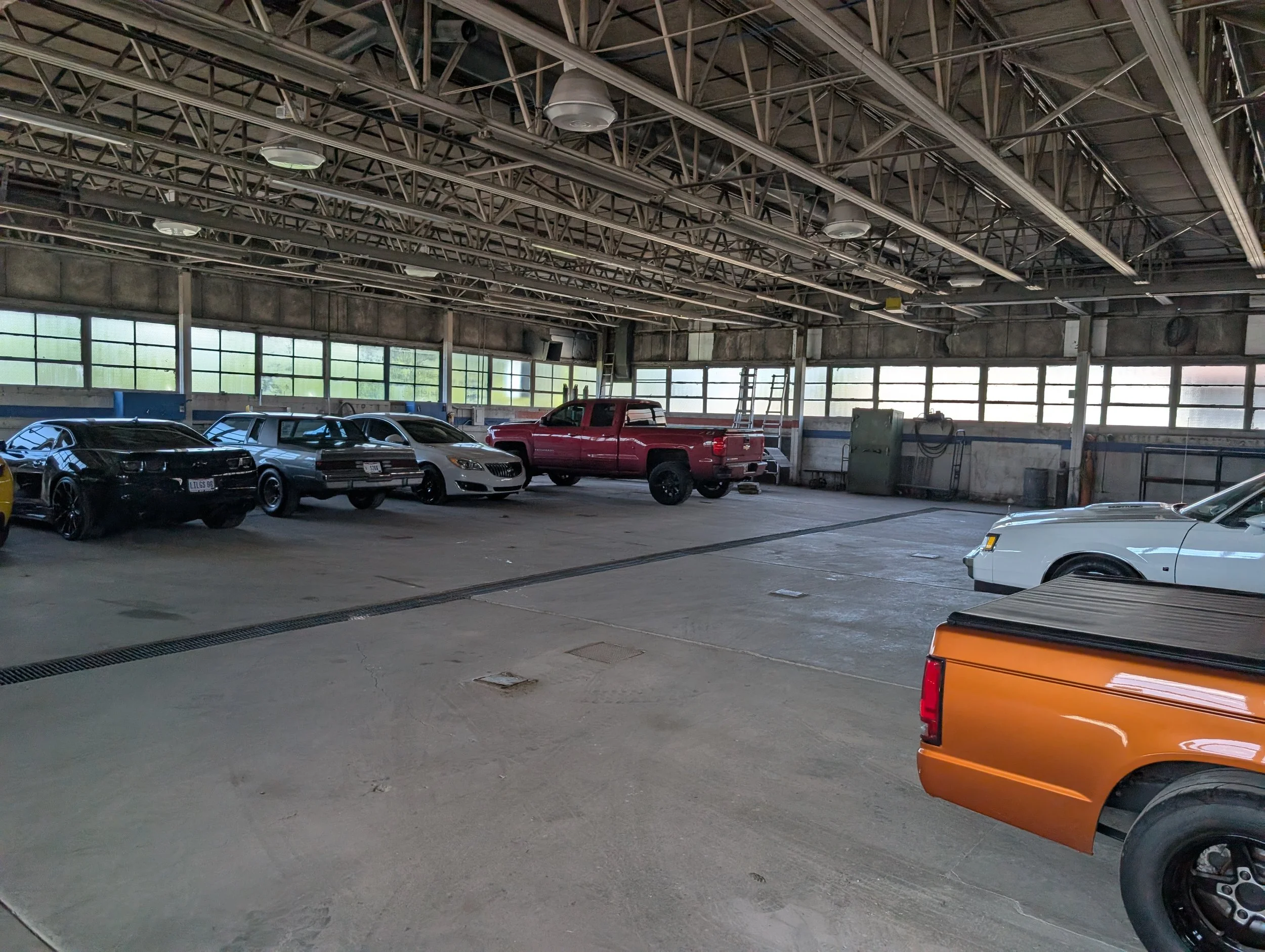 Indoor parking garage with several parked cars, concrete floor, and metal ceiling structure with lights and support beams.