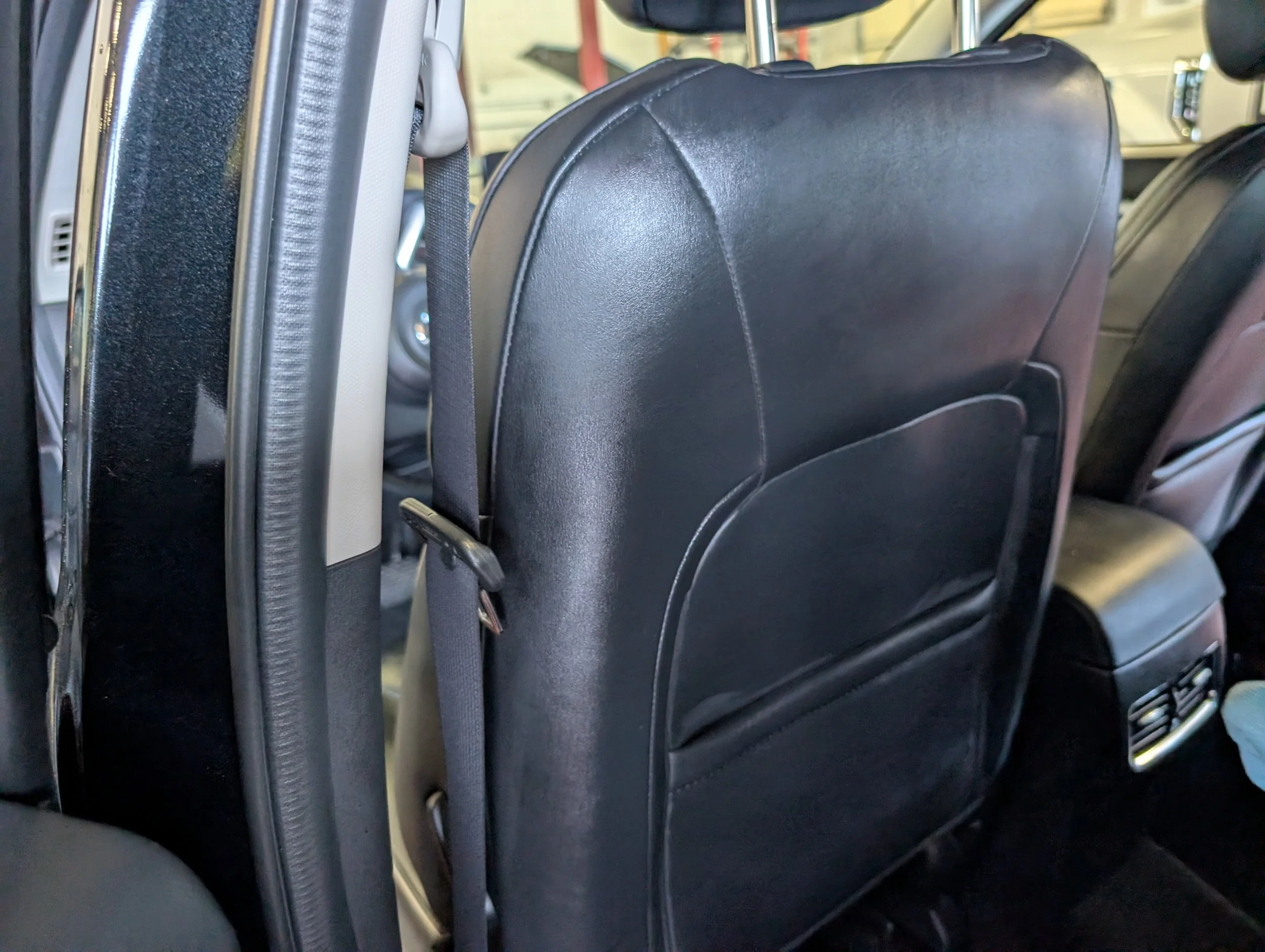Inside a bus, showing the back of black leather seats with a strap attached for holding on during travel.