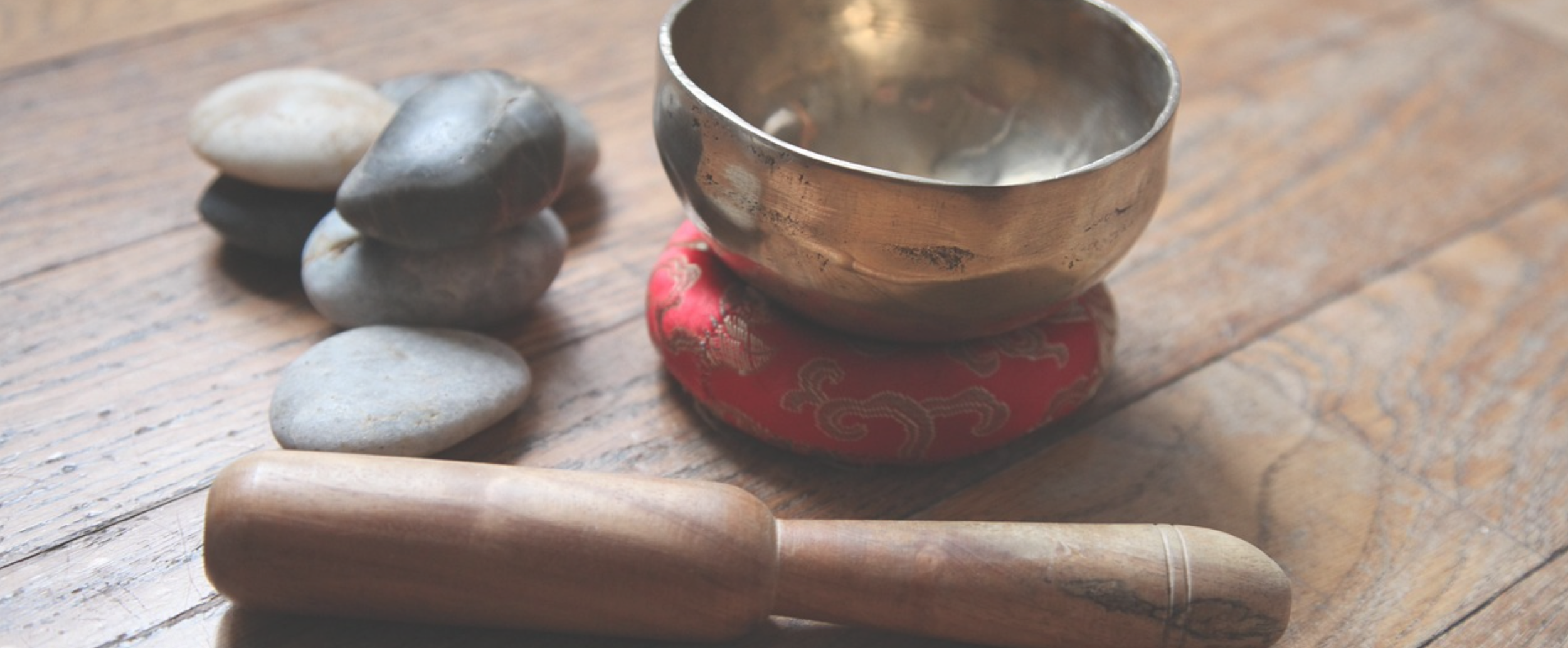 A set of rocks, a singing bowl on a red cushion, and a wooden mallet arranged on a wooden surface.